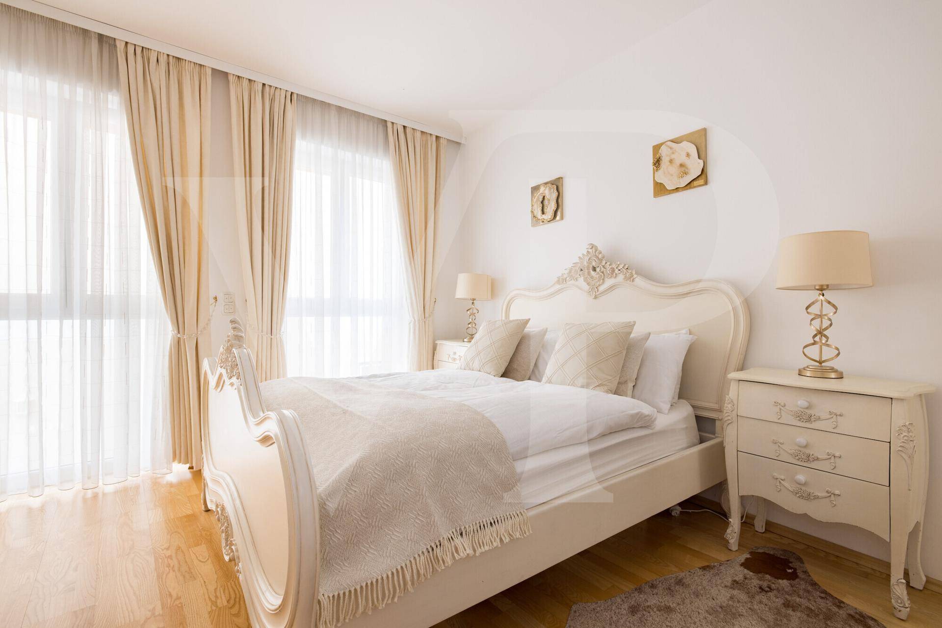 Geräumiges Schlafzimmer mit großem weißem Bett, Nachttischen und viel Tageslicht durch die Fenster.