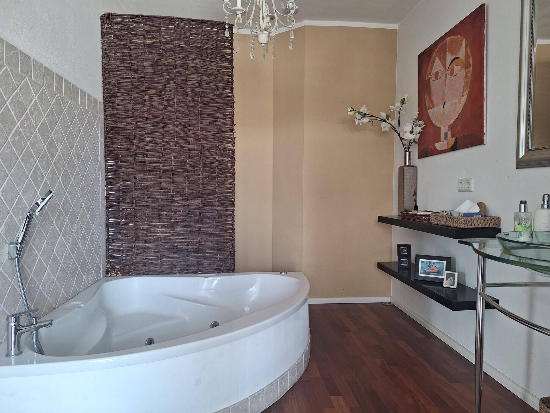 Geräumiges Badezimmer mit Eckbadewanne, Holzboden und elegantem Kronleuchter.