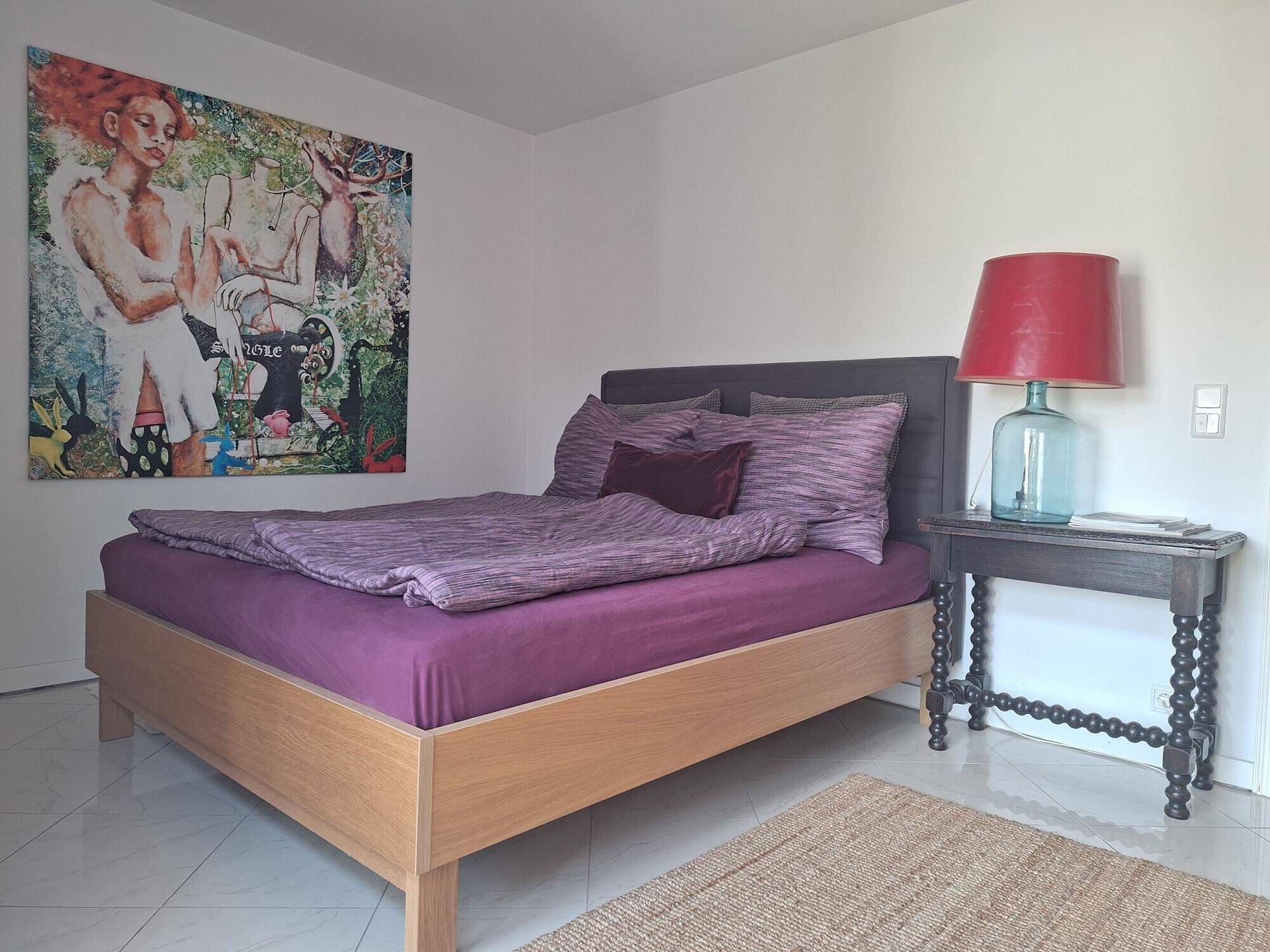 Gemütliches Schlafzimmer mit Doppelbett, Nachttisch und farbenfrohem Kunstwerk.