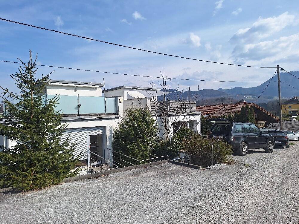 Außenansicht des modernen Gebäudes mit Flachdach, Parkplätzen und Bergblick im Hintergrund.