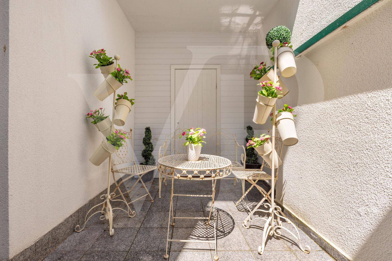 Gemütliche Loggia mit kleinem Tisch und Stühlen, dekoriert mit Blumen, ideal zum Entspannen.