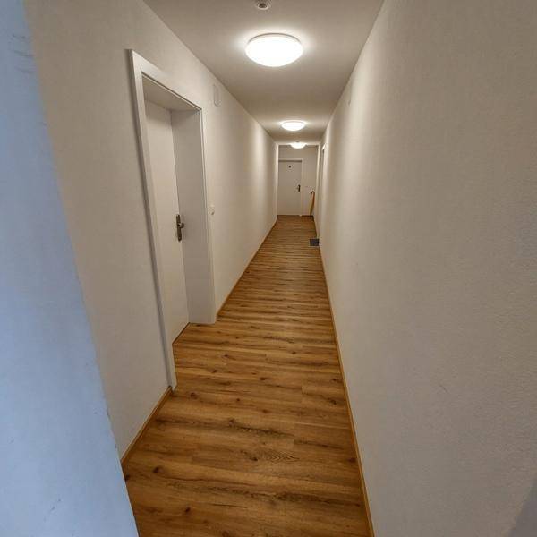 Langer, heller Flur mit Laminatboden und mehreren Türen zu den Zimmern.