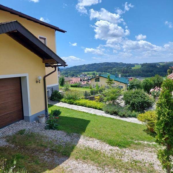 Seitenansicht des Hauses mit Garage, Rasenfläche und weitem Blick auf die umliegende Landschaft.