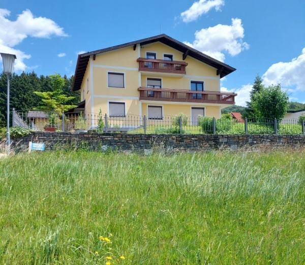 Ansicht des gelben Wohnhauses mit zwei Balkonen, umgeben von einer Wiese und Bäumen.