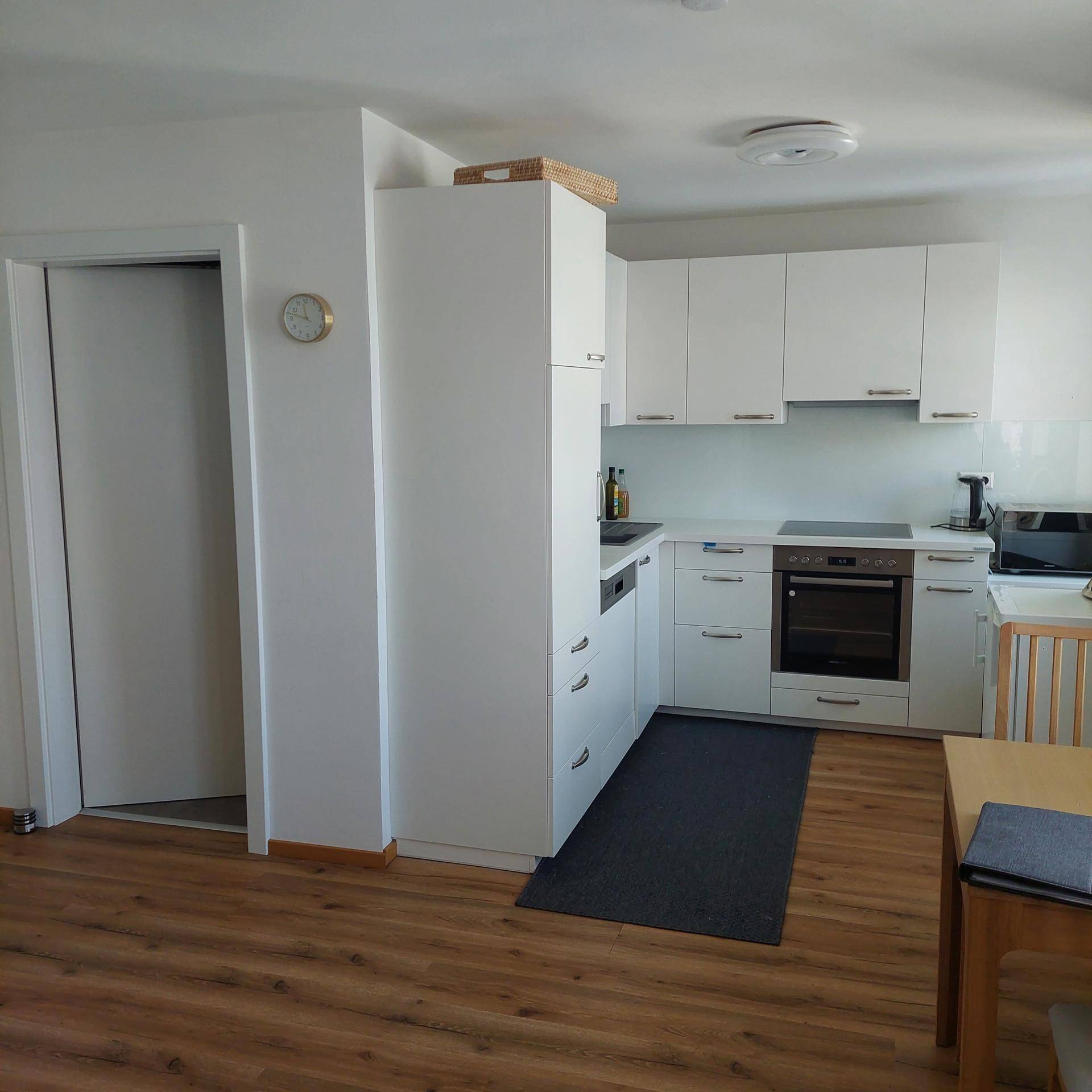 Moderne Einbauküche mit weißen Schränken, integrierten Geräten und Laminatboden.