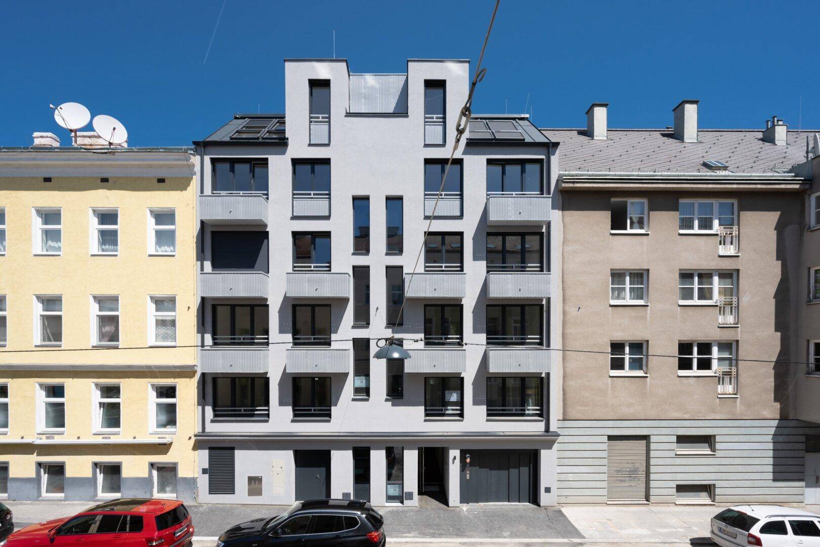 Moderne Gebäudefassade mit vielen Fenstern und Balkonen in einer urbanen Umgebung.