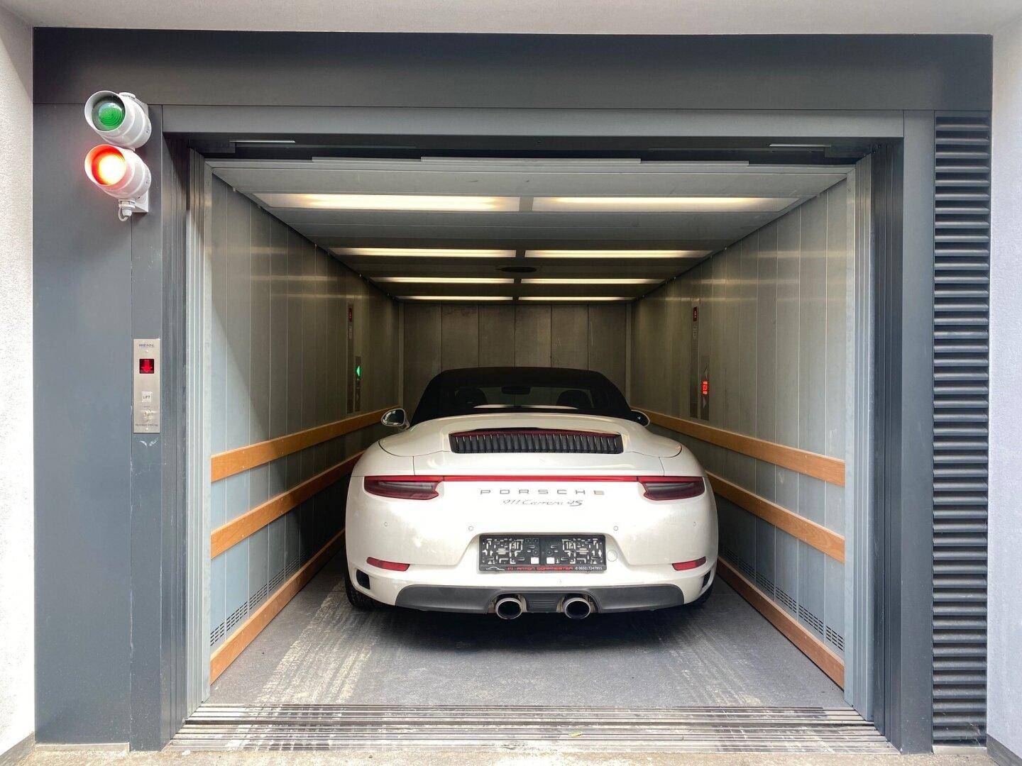 Ein weißer Sportwagen steht im modernen Autoaufzug bereit zur Fahrt in die Tiefgarage.