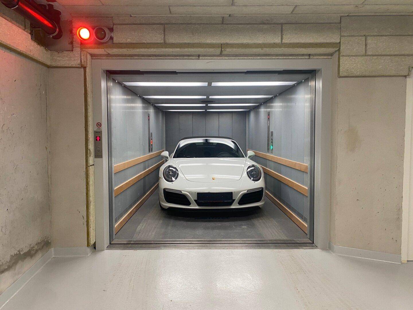 Ein weißer Sportwagen steht im Autoaufzug, bereit zur Einfahrt in die Tiefgarage.