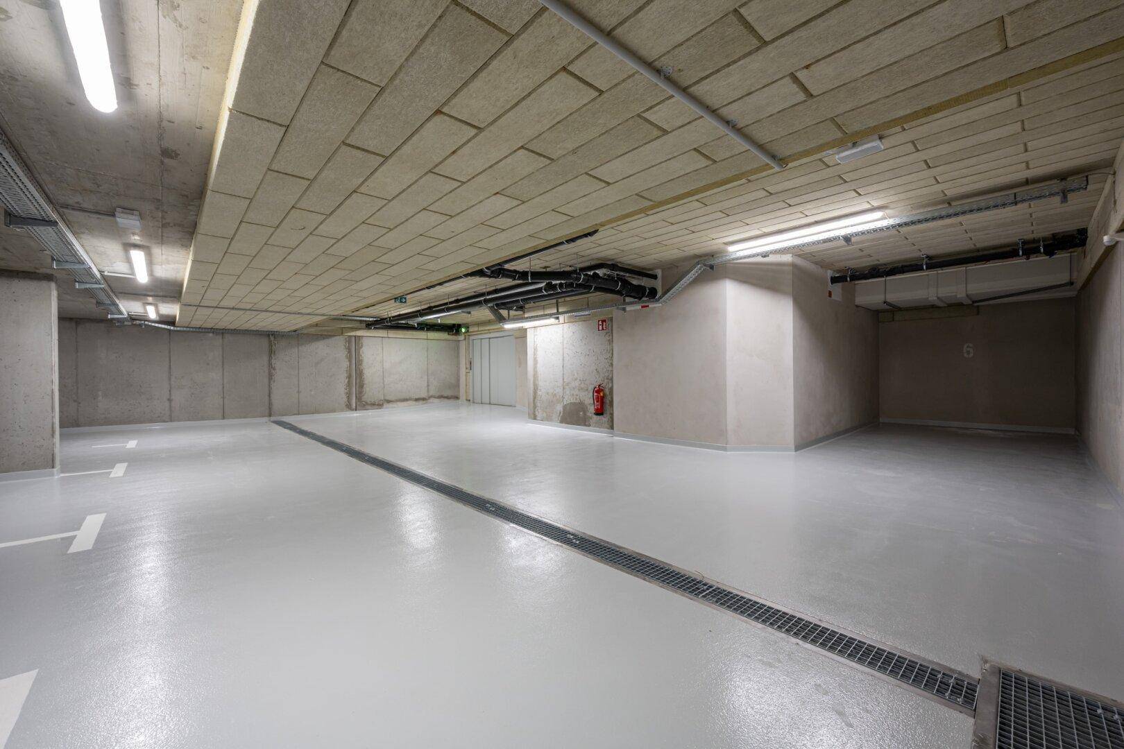 Geräumige Tiefgarage mit markierten Stellplätzen, Entwässerungsrinne und moderner Beleuchtung.