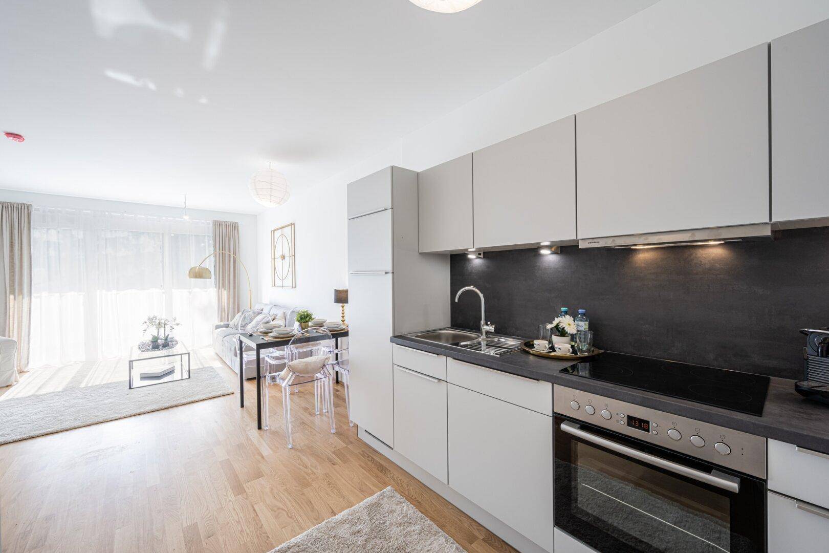 Moderne Einbauküche in Grau mit Kochfeld und Backofen im offenen Wohnbereich.