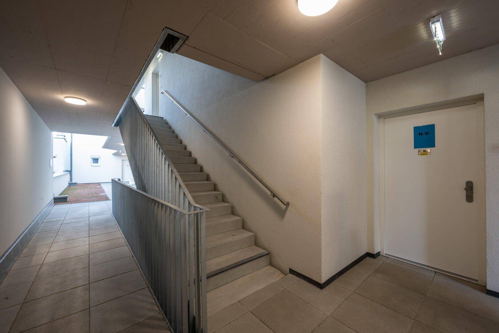 Heller Treppenaufgang mit Fliesenboden und Geländer in einem Mehrfamilienhaus.