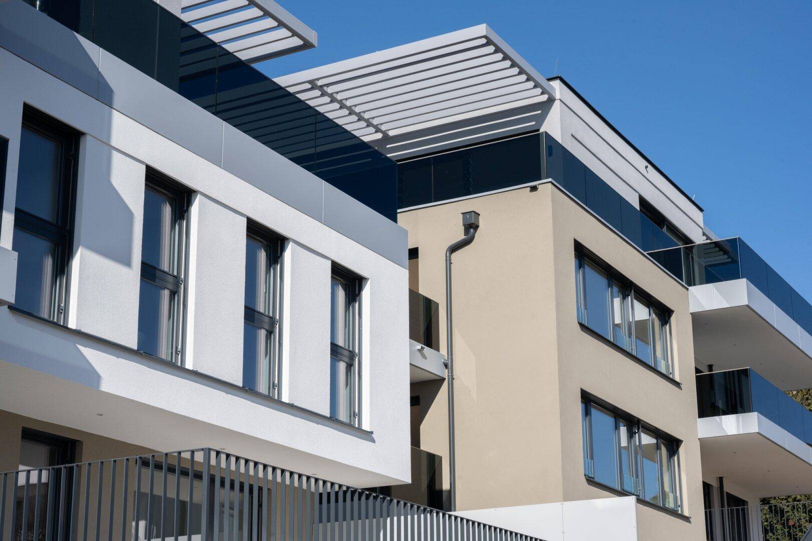 Moderne Architektur eines Mehrfamilienhauses mit Balkonen und klaren Linien unter blauem Himmel.
