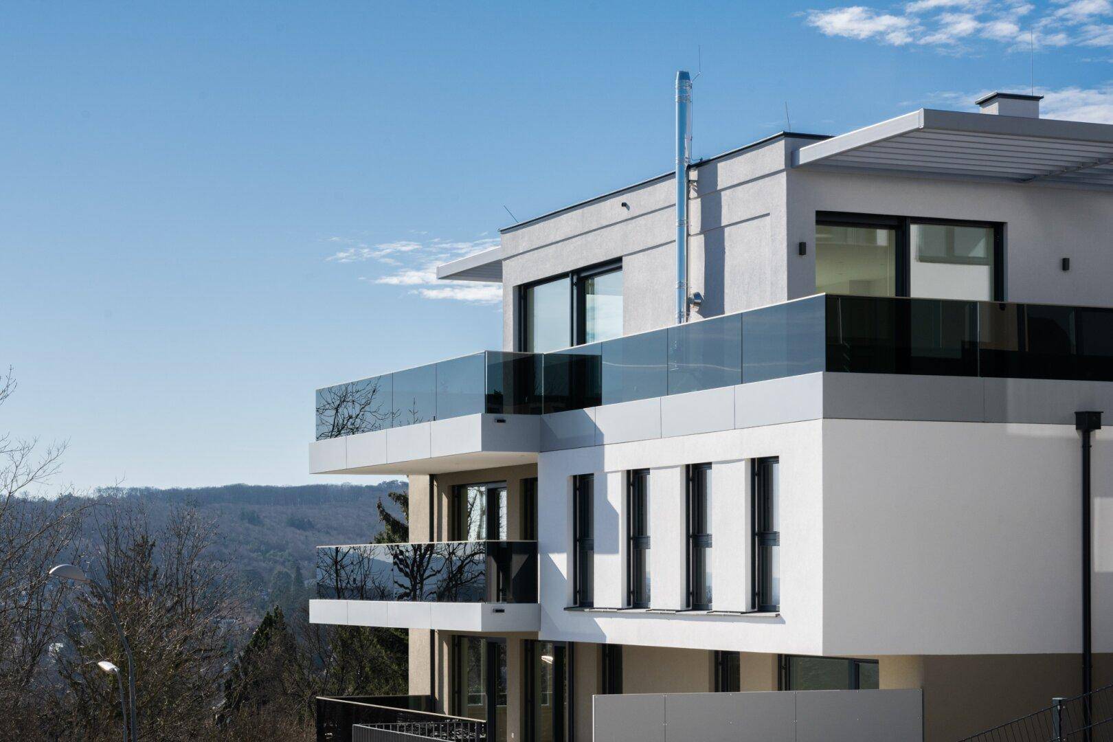 Elegantes Mehrfamilienhaus mit Glasbalkonen und Panoramablick auf die umliegende Landschaft.