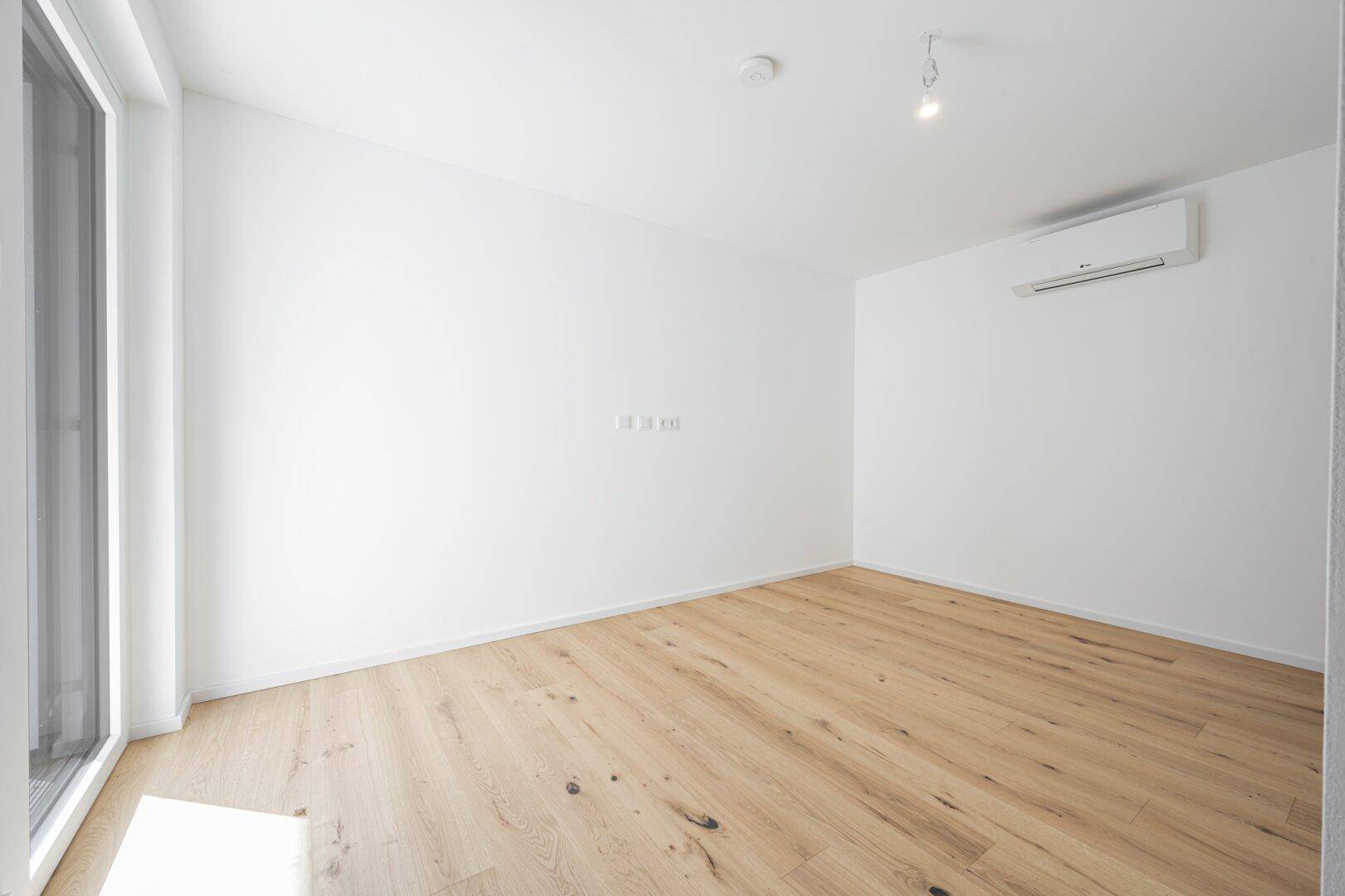 Geräumiges Zimmer mit Holzboden und Klimaanlage, ideal für Schlaf- oder Arbeitsbereich.