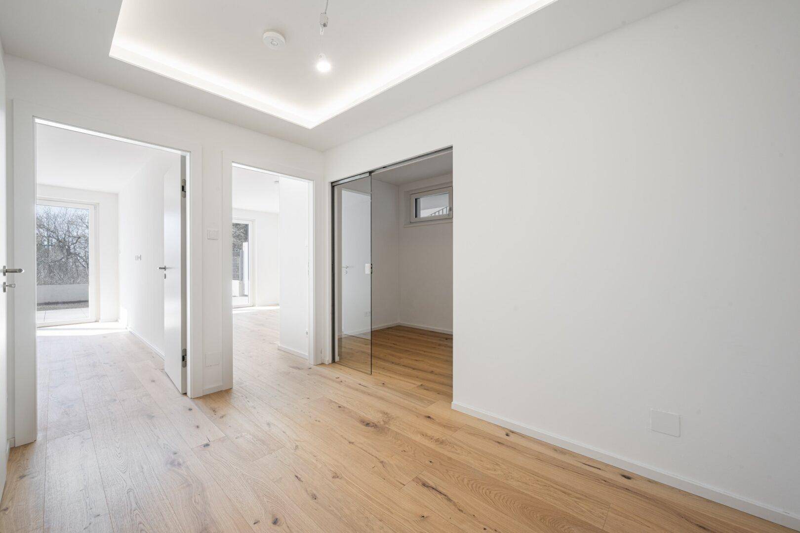 Moderner Flur mit Holzboden und Schiebetür aus Glas, die Räume elegant verbindet.
