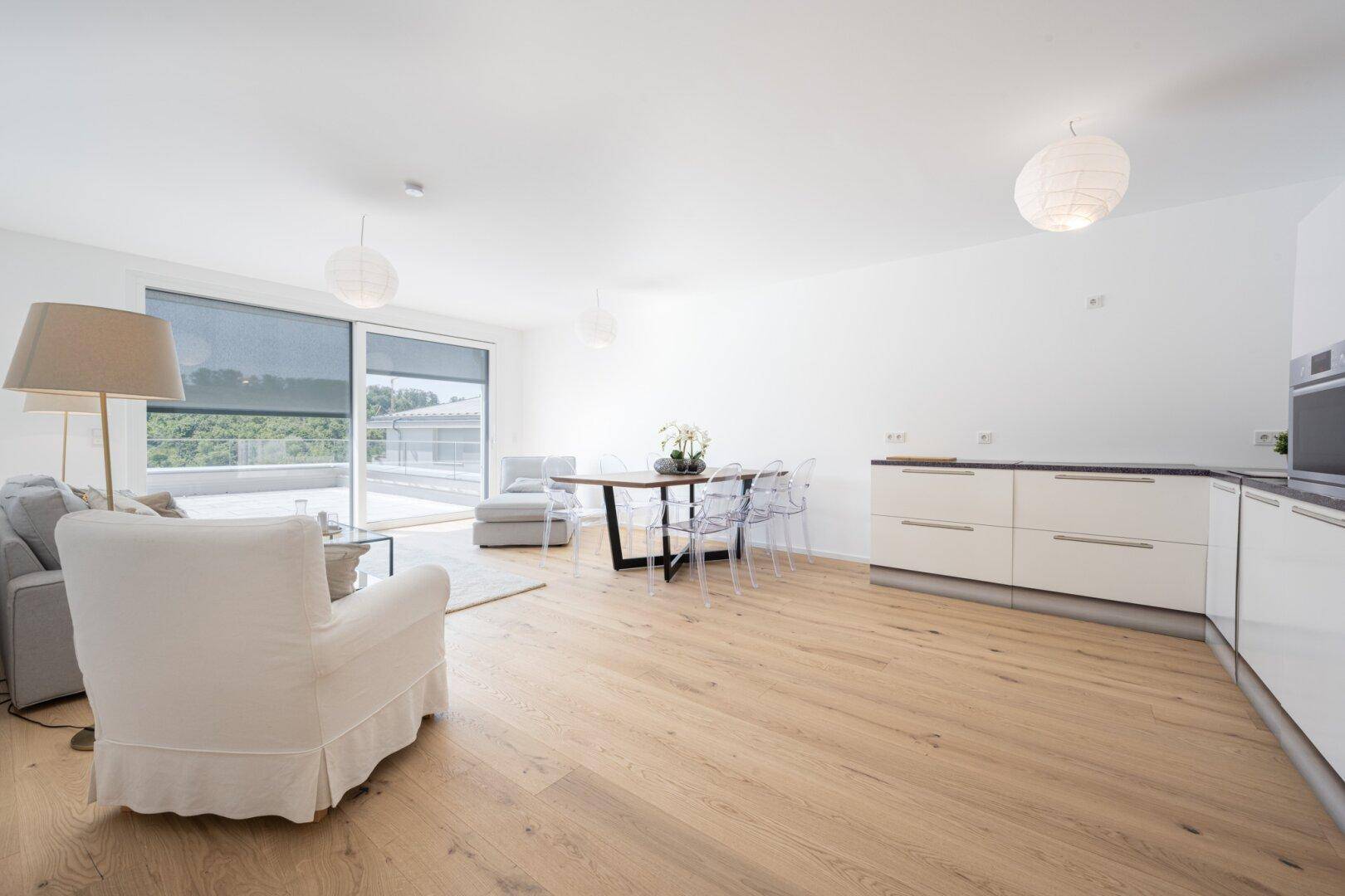 Geräumiger Wohn-Essbereich mit integrierter Küchenzeile, Holzboden und Zugang zu einer Terrasse.