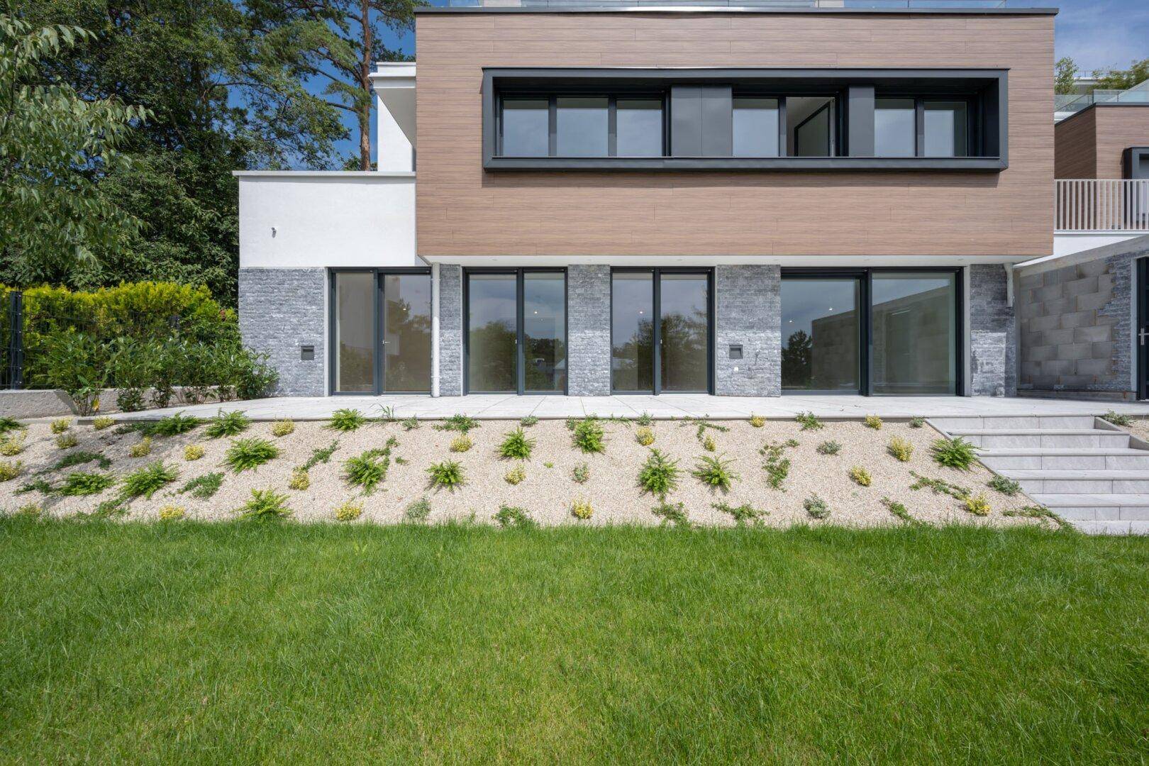 Terrasse im Erdgeschoss mit Zugang zum Garten und großen Fensterfronten des modernen Gebäudes.