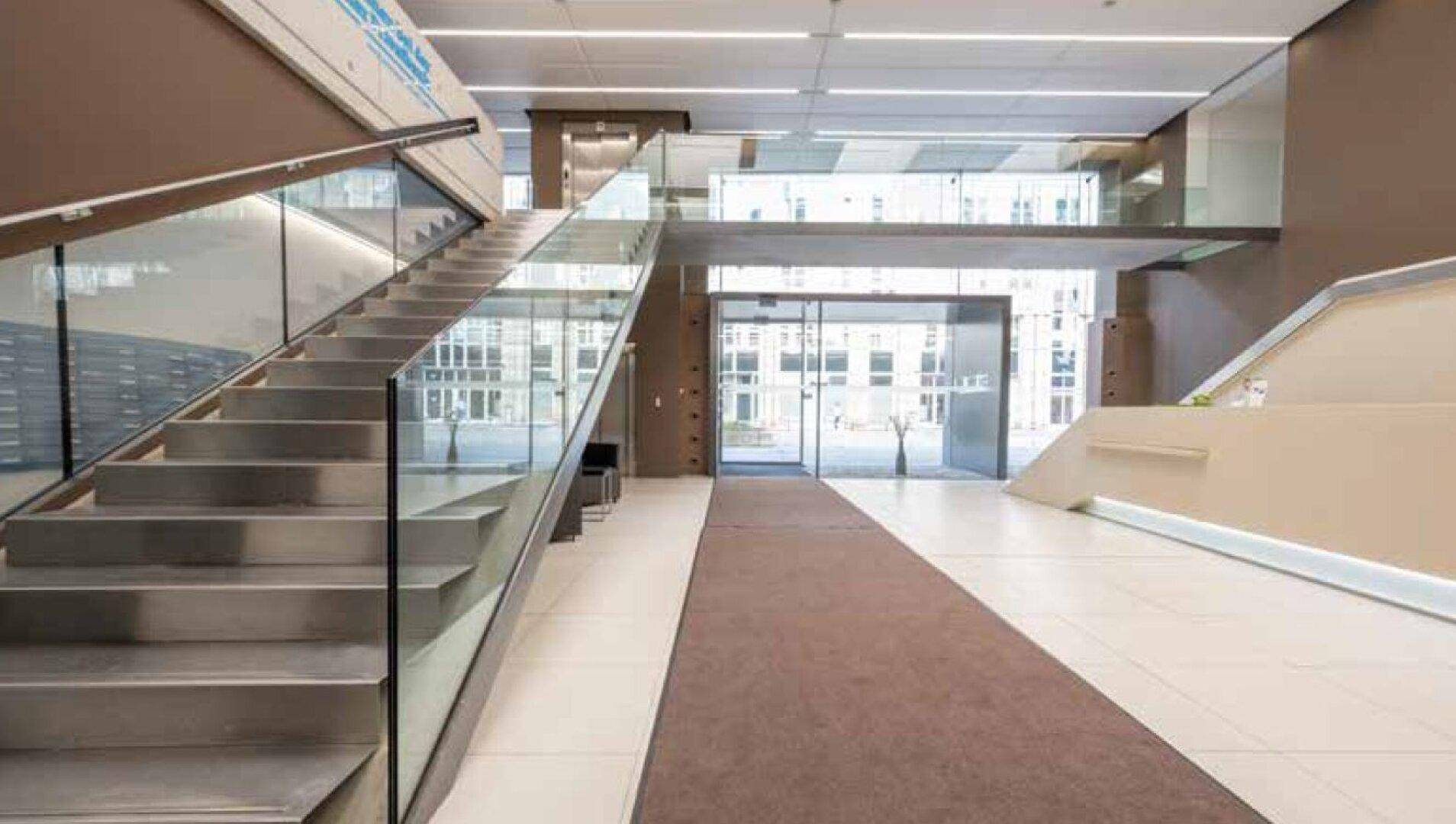 Modernes Treppenhaus mit Glasgeländer und hellem Eingangsbereich in einem Geschäftsgebäude.