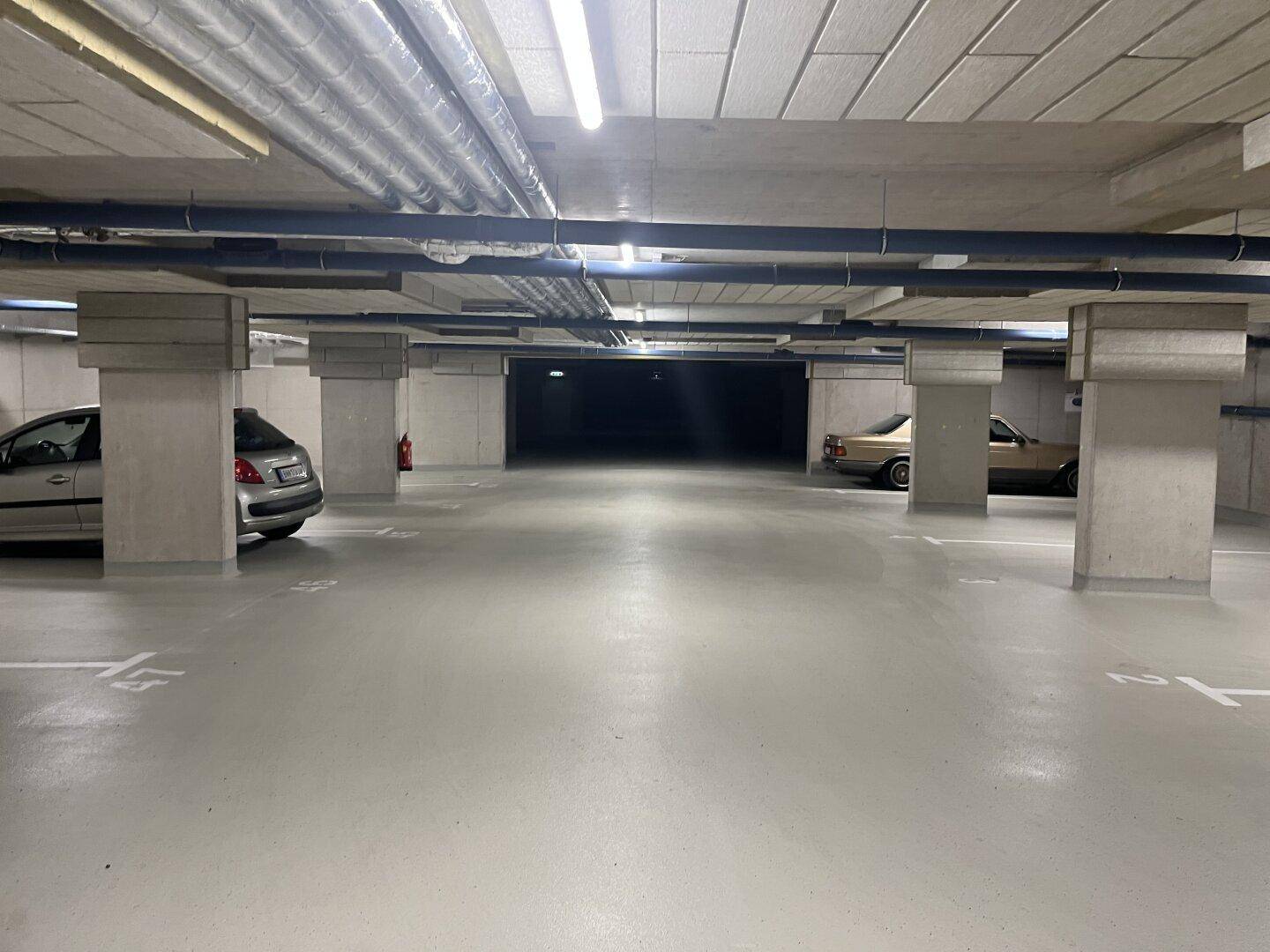 Geräumige Tiefgarage mit Betonstützen, Beleuchtung und mehreren Stellplätzen für Fahrzeuge.