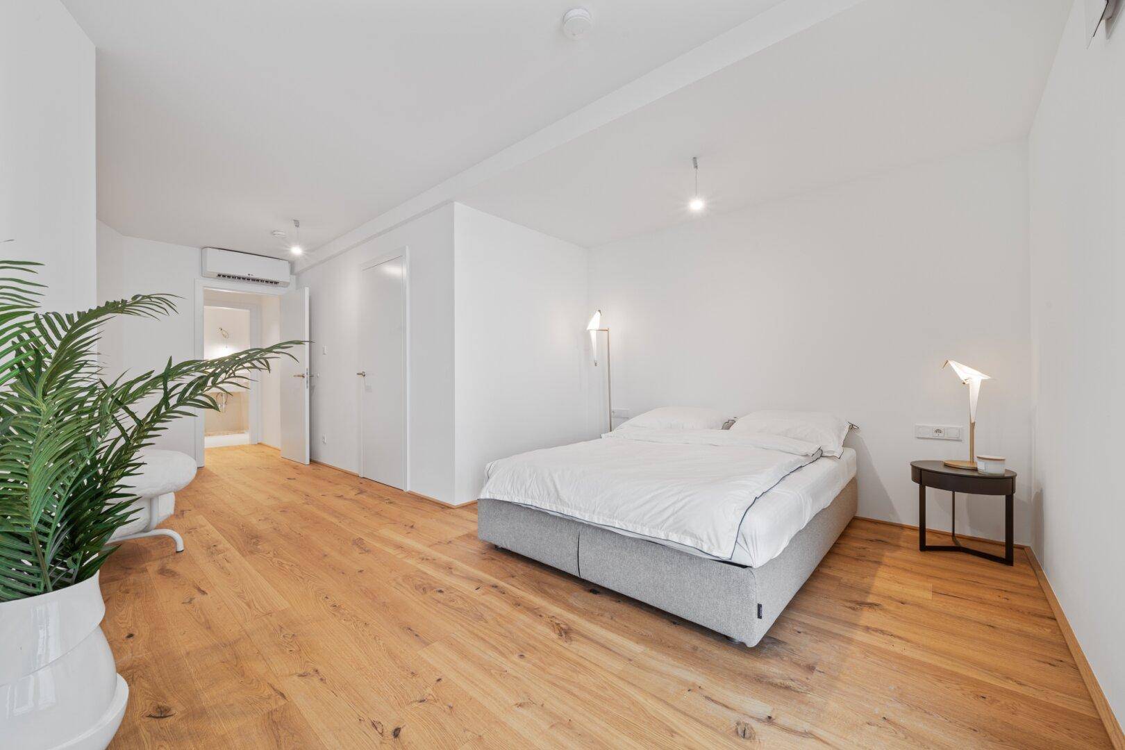 Helles Schlafzimmer mit Holzboden, Doppelbett und Klimaanlage, mit Zugang zum Badezimmer.