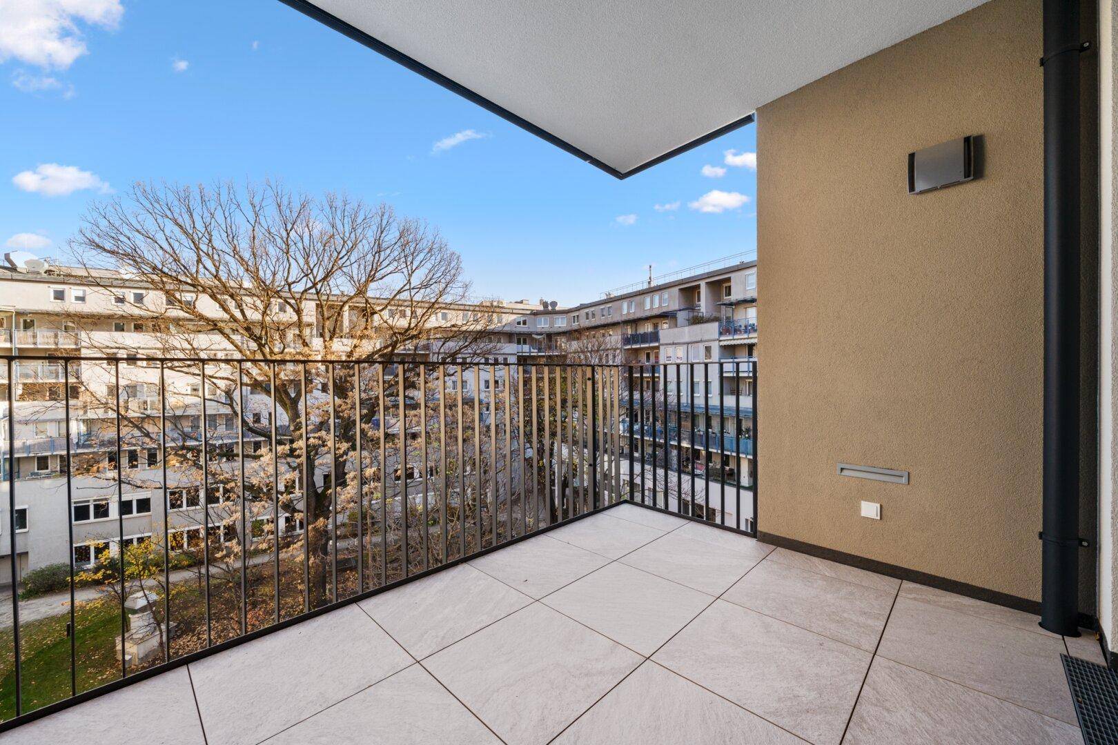 Geräumiger Balkon mit Fliesenboden und Blick auf den begrünten Innenhof der Wohnanlage.