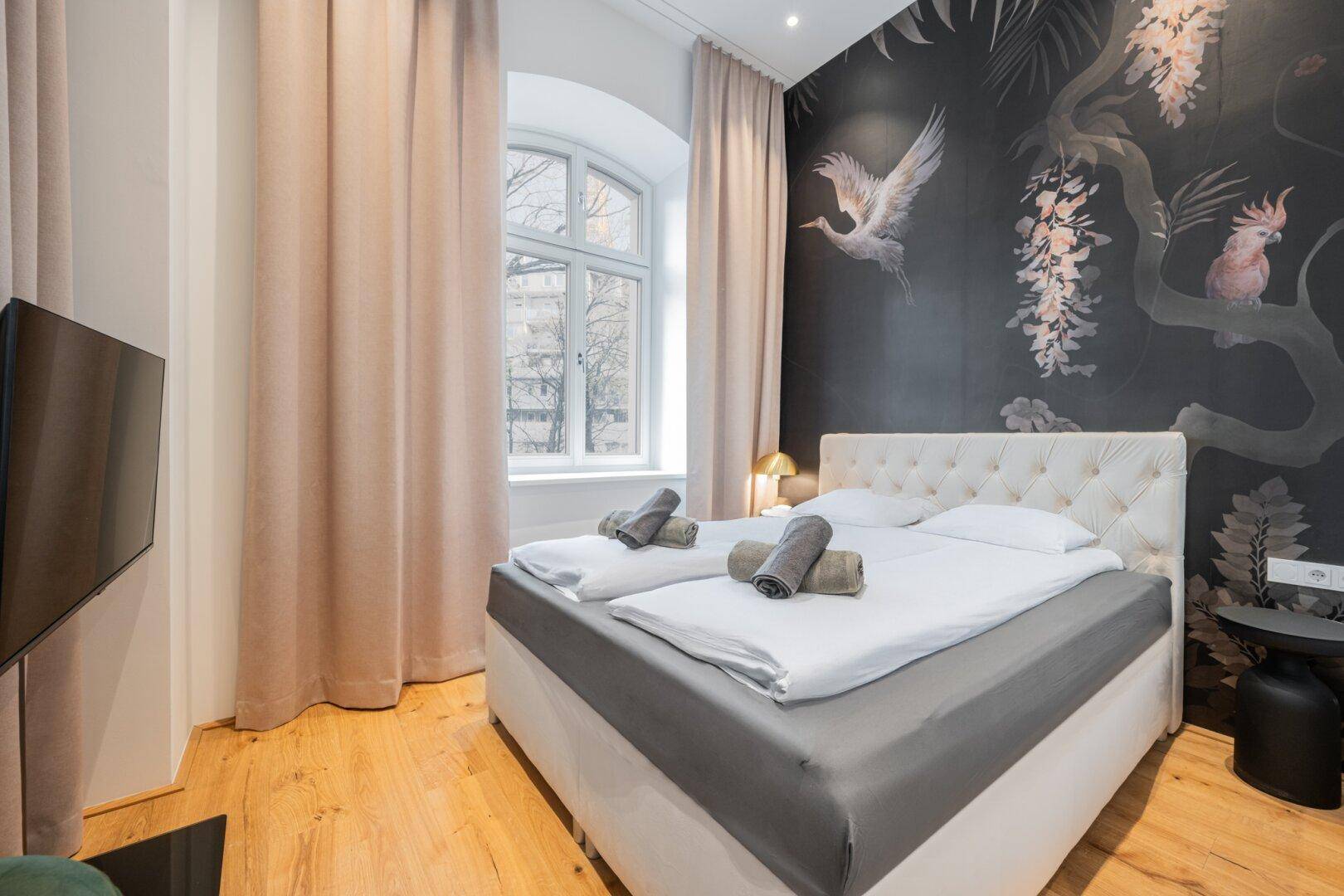 Gemütliches Schlafzimmer mit Doppelbett, Holzboden und einer auffälligen Wandtapete mit Vogelmotiv.
