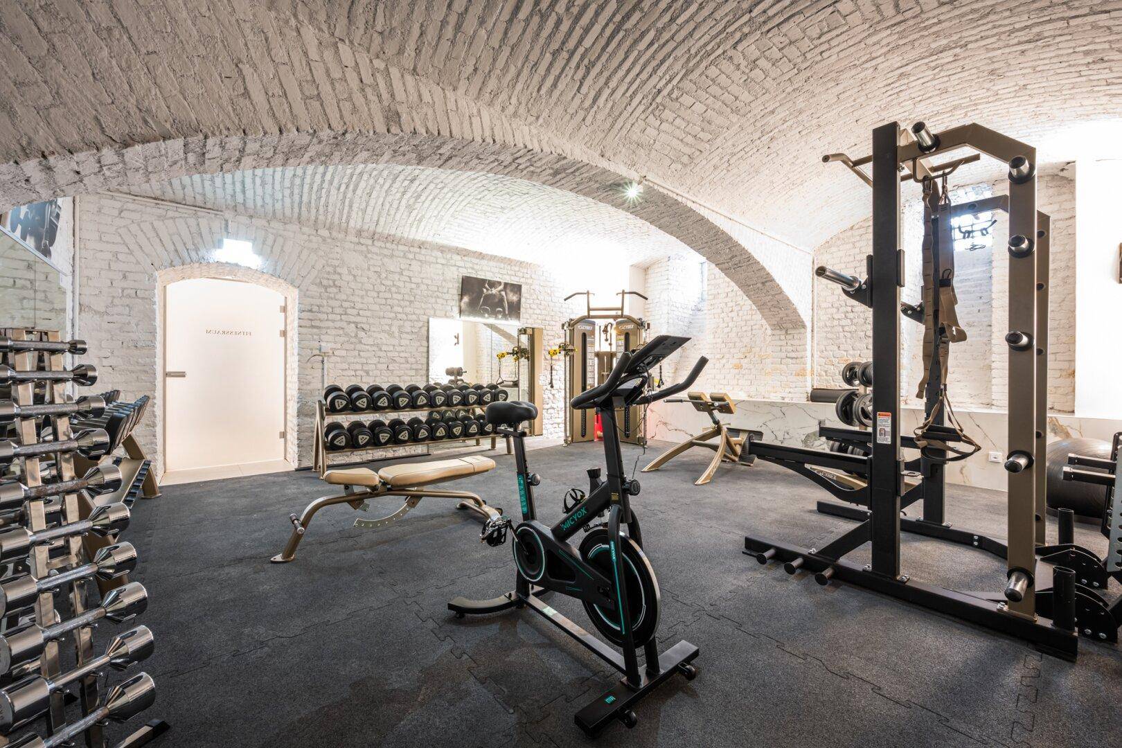 Gut ausgestatteter Fitnessraum im Gewölbekeller mit verschiedenen Geräten und Hanteln.