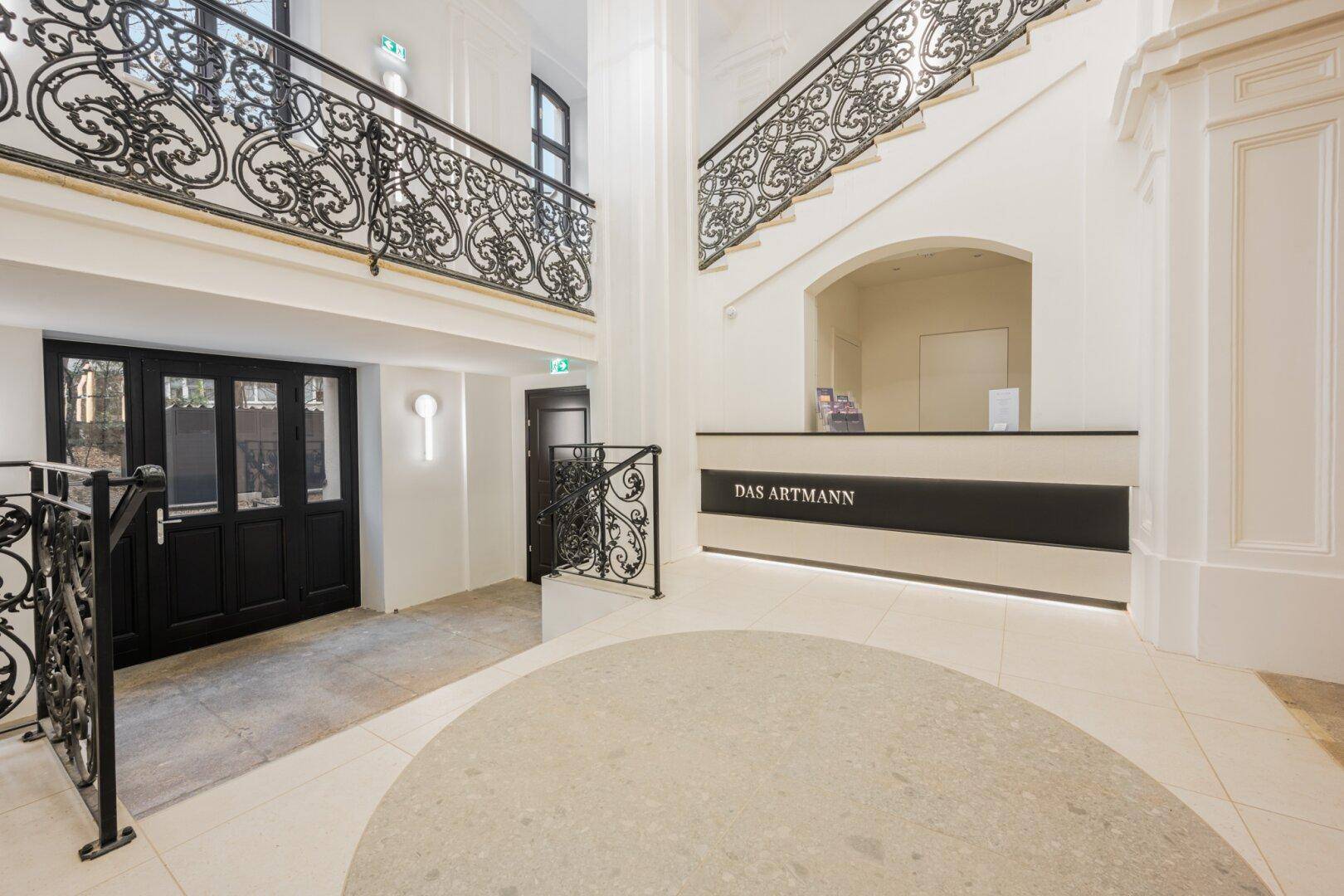 Eleganter Eingangsbereich mit Concierge-Schalter, geschwungenen Treppen und schmiedeeisernen Geländern.