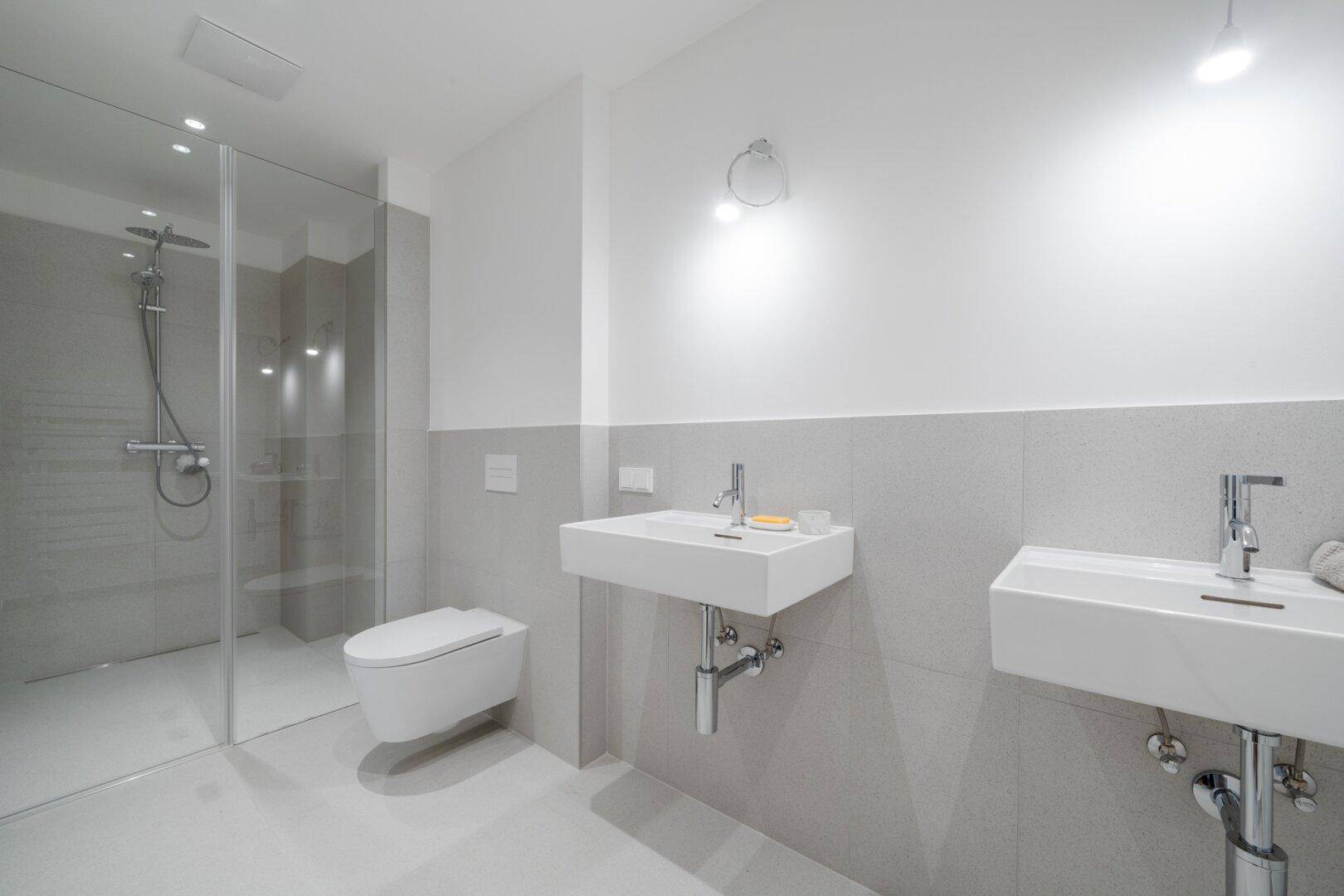 Modernes Badezimmer mit begehbarer Dusche, Doppelwaschbecken und Wand-WC in hellen Grautönen.