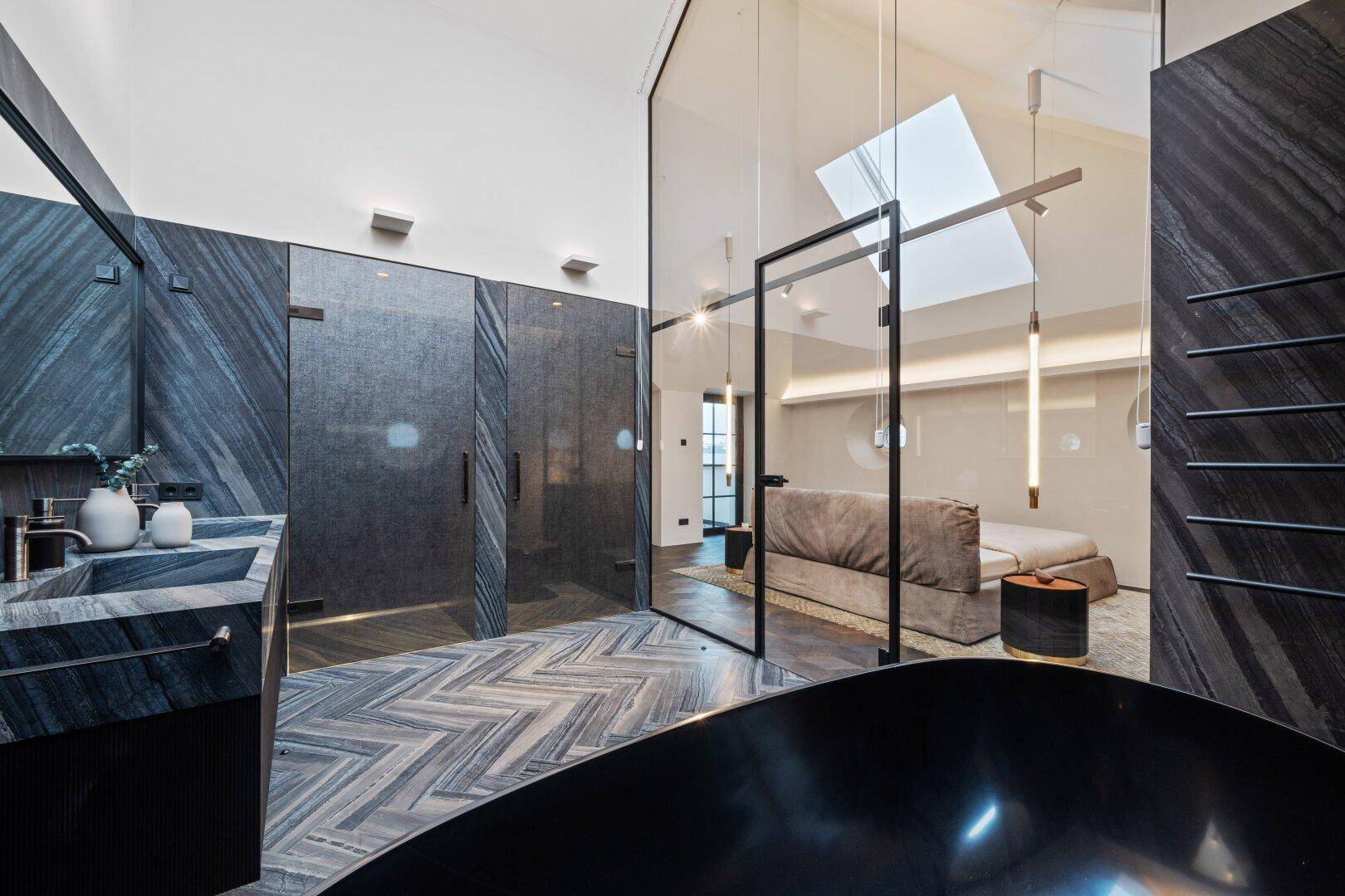 Luxuriöses Badezimmer mit dunklen Steinwänden, freistehender Badewanne und offener Verbindung zum Schlafzimmer.