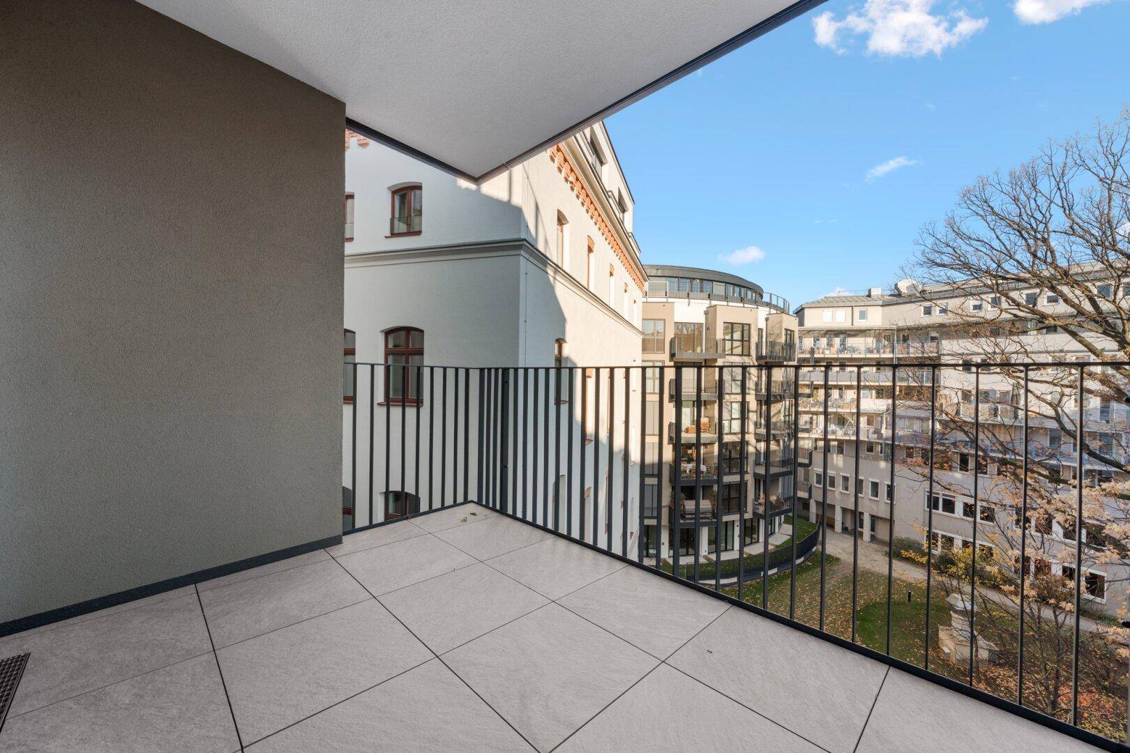 Geräumiger Balkon mit Fliesenboden und Blick auf die umliegenden Gebäude und den Innenhof.