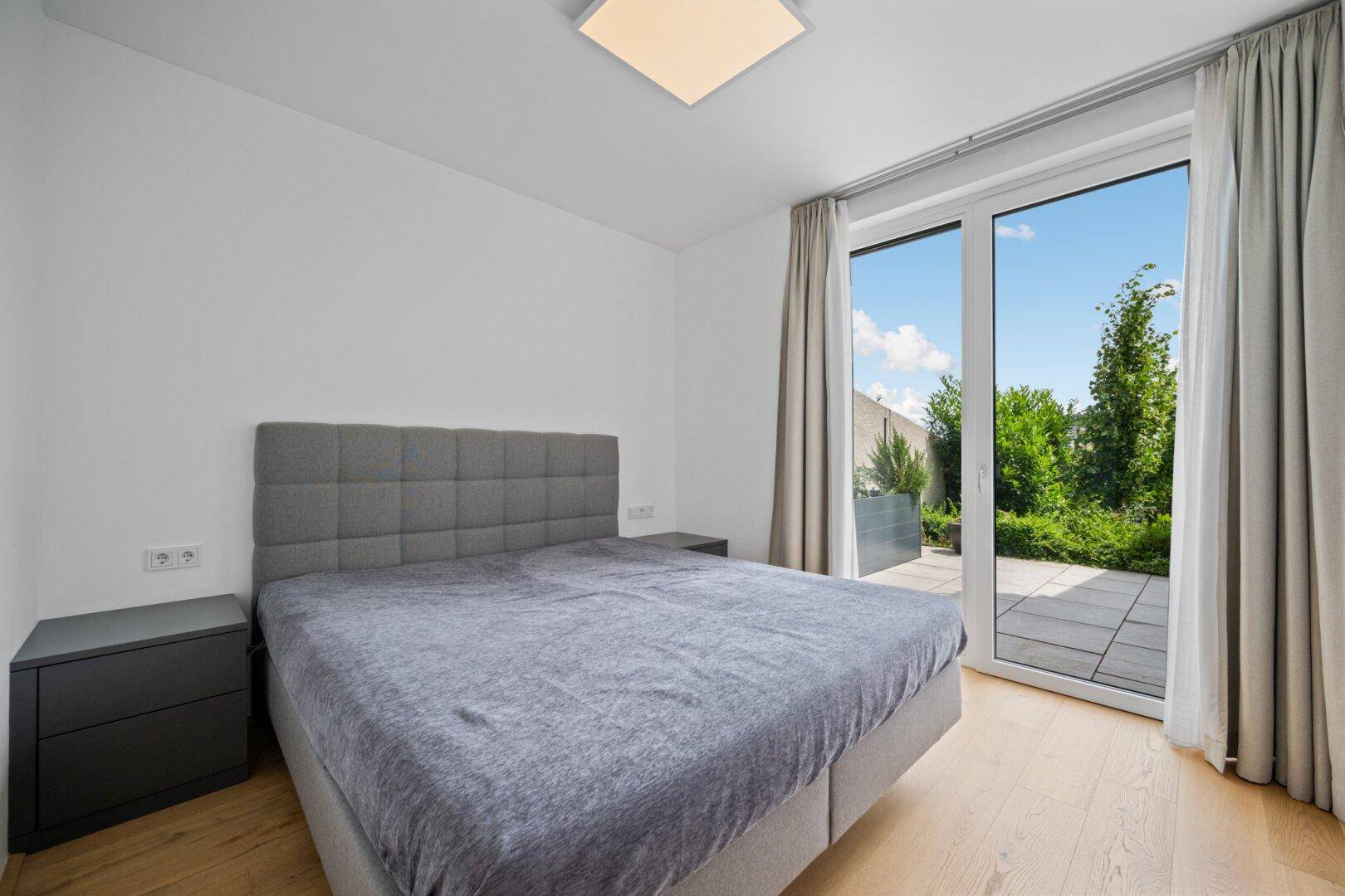 Helles Schlafzimmer mit Doppelbett, Nachttischen und Zugang zur Außenterrasse.