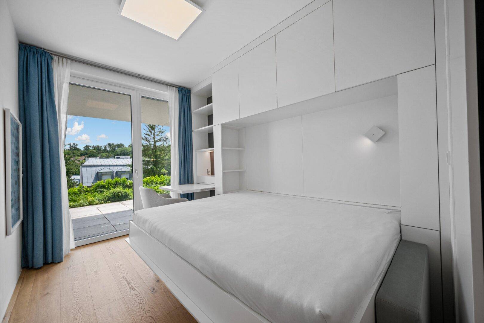 Helles Schlafzimmer mit integriertem Schreibtisch, Stauraum und Terrassenzugang.