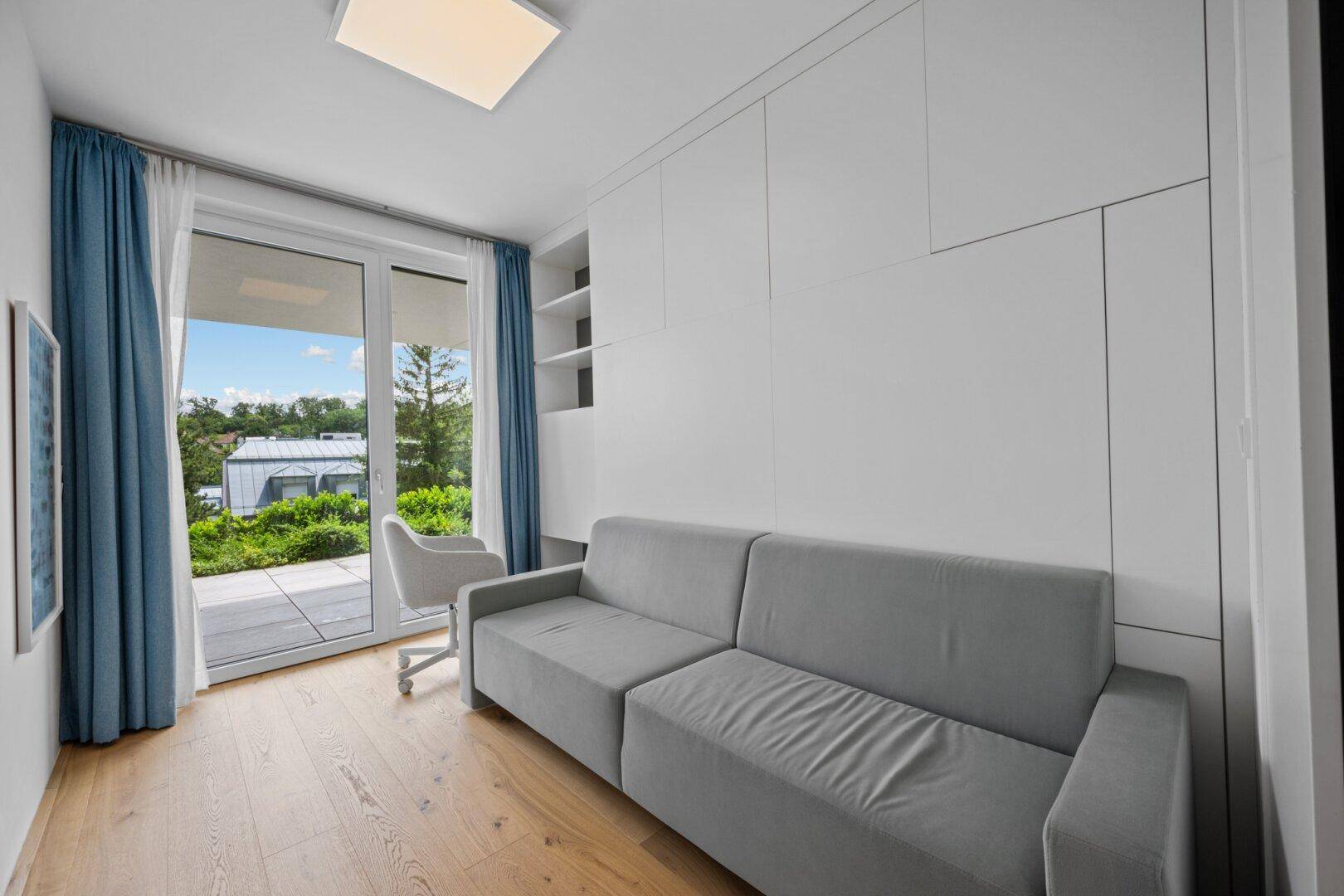 Heller Raum mit grauem Sofa, Einbauschränken und Zugang zur Terrasse.