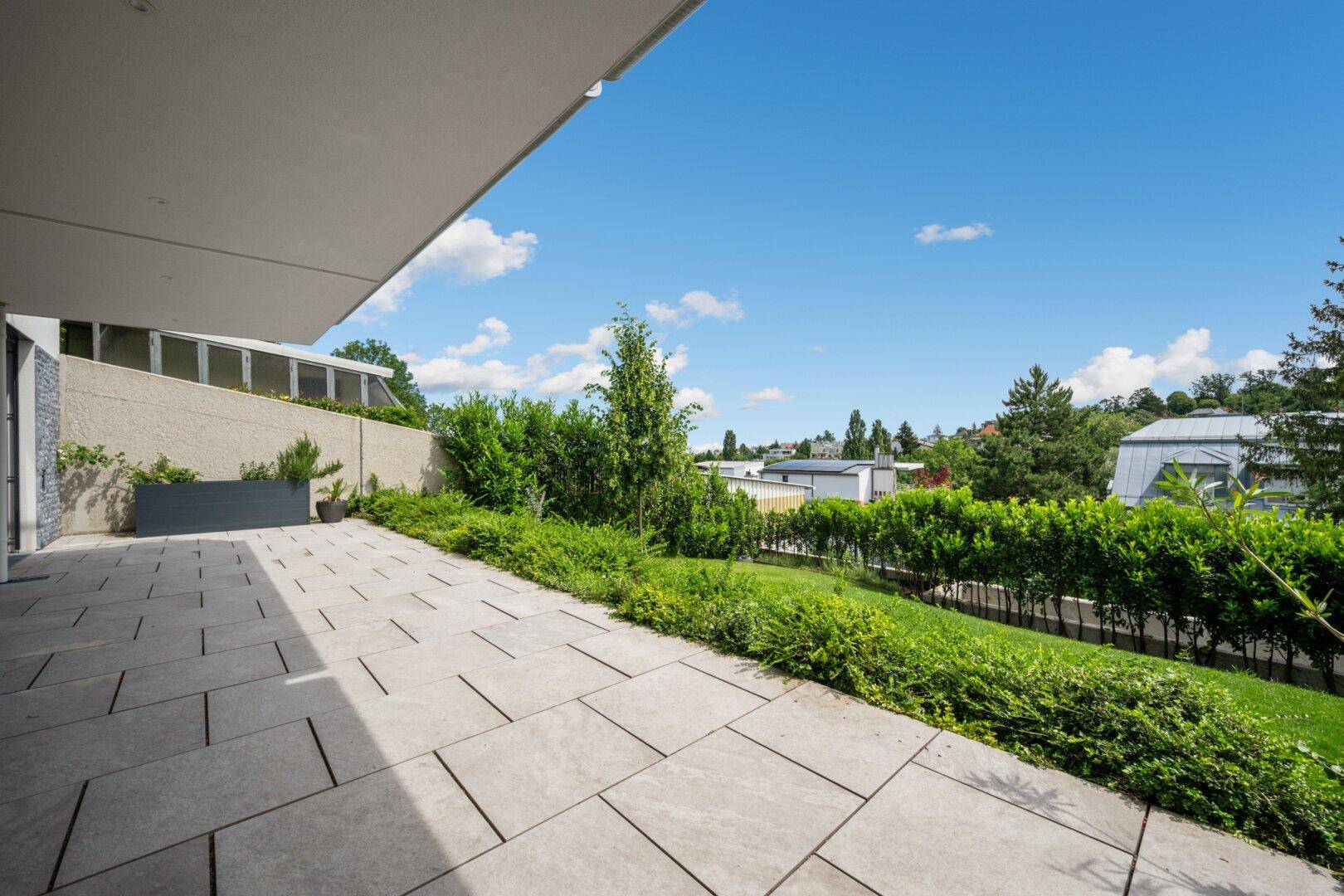 Große gepflasterte Terrasse mit Grünflächen und Blick auf die Umgebung.