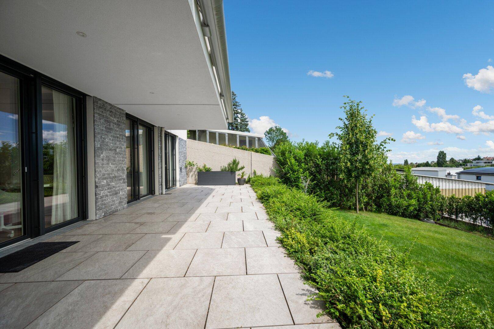 Weitläufige Terrasse mit Steinplatten und angrenzendem Gartenbereich, ideal zum Entspannen.