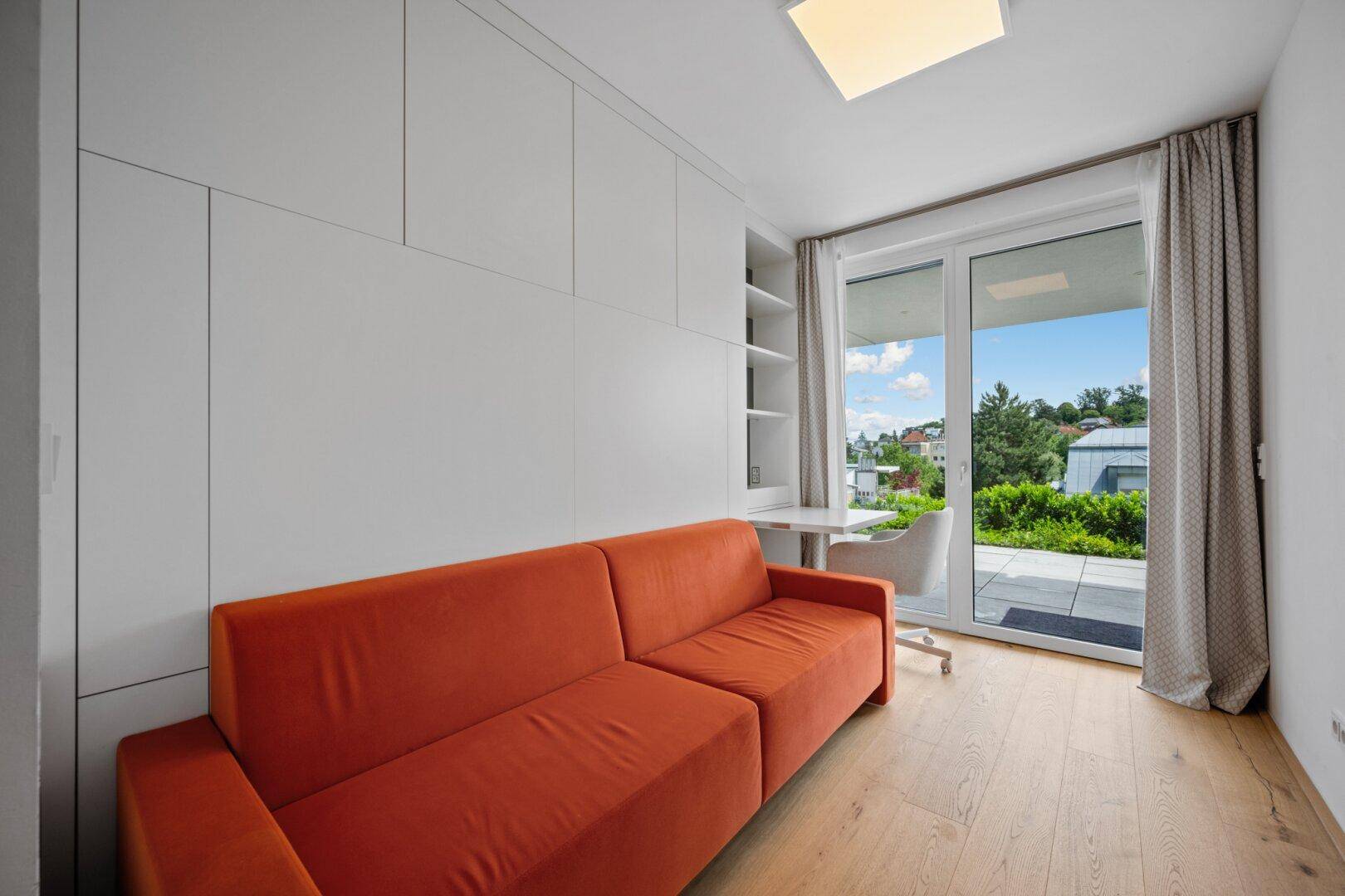 Heller Raum mit orangefarbenem Sofa, Einbauschränken und Zugang zur Terrasse.