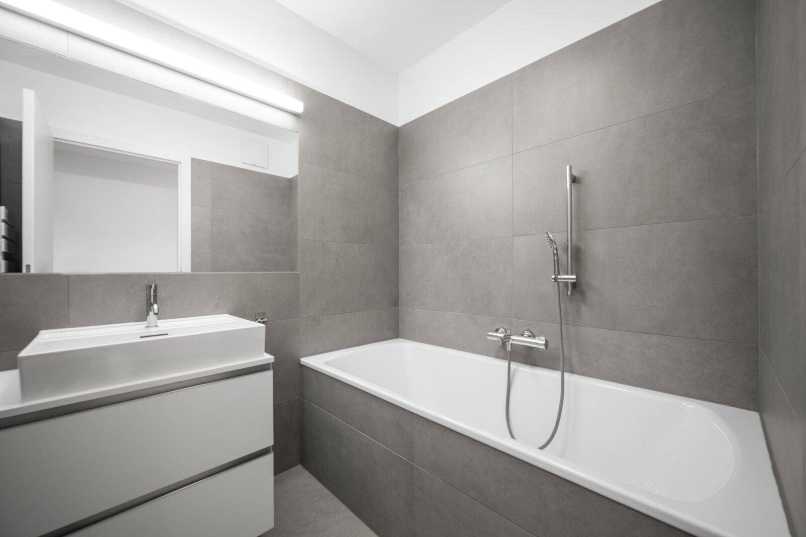 Modernes Badezimmer mit Badewanne, Waschtisch und grauen Wandfliesen.