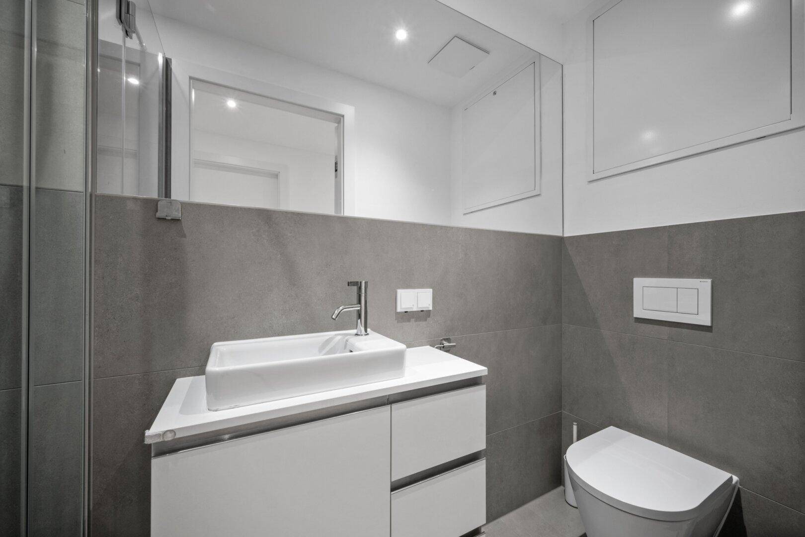 Modernes Gäste-WC mit Waschtisch, Spiegel und Wand-WC in minimalistischem Design.