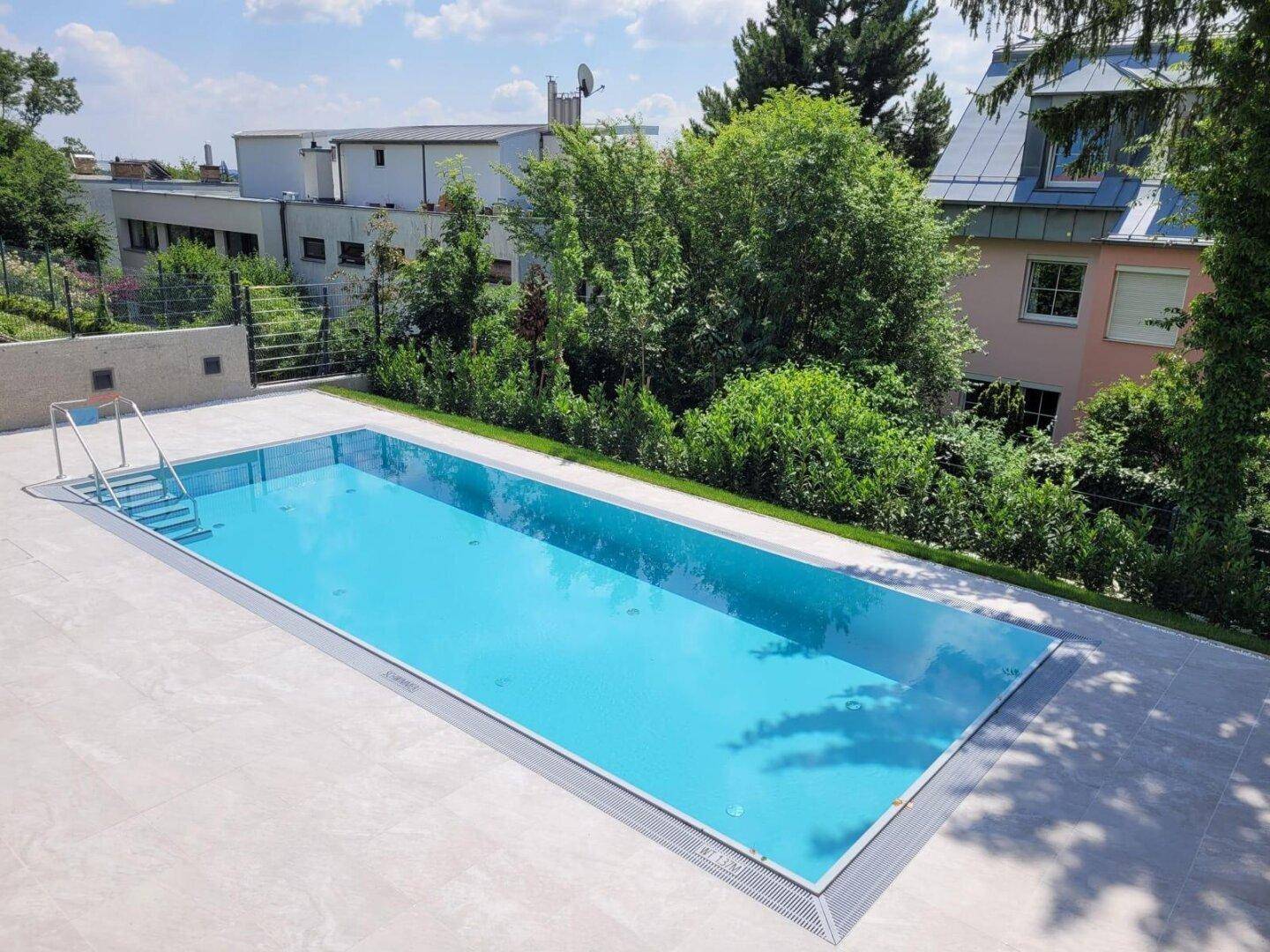 Großer Außenpool mit umliegender Terrasse und Blick auf die grüne Umgebung.