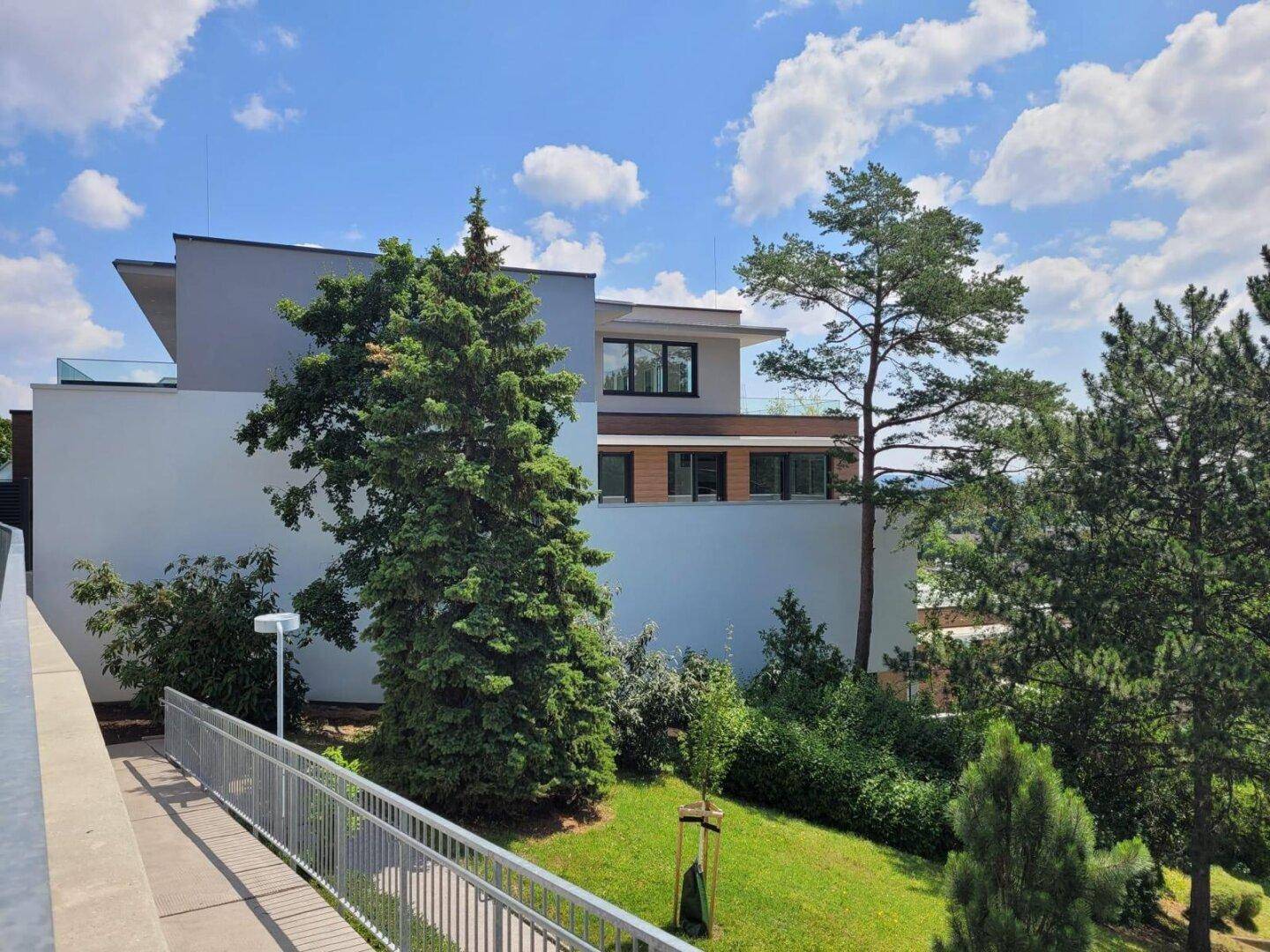 Moderne Architektur des Gebäudes mit mehreren Ebenen und viel Grün in der Umgebung.
