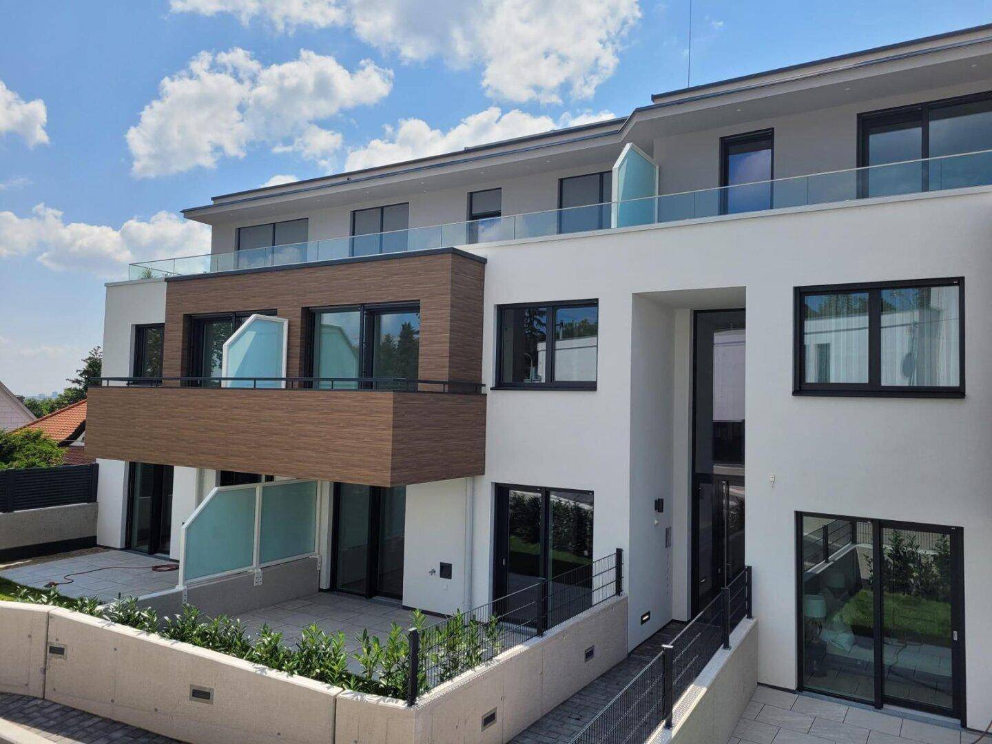 Elegante Fassade eines Neubaus mit Balkonen, Terrassen und großen Fensterfronten.