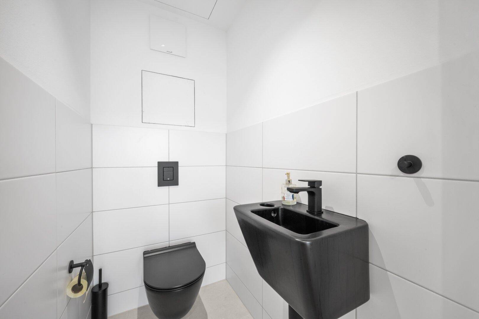 Modernes Gäste-WC mit schwarzen Armaturen und weiß gefliesten Wänden.