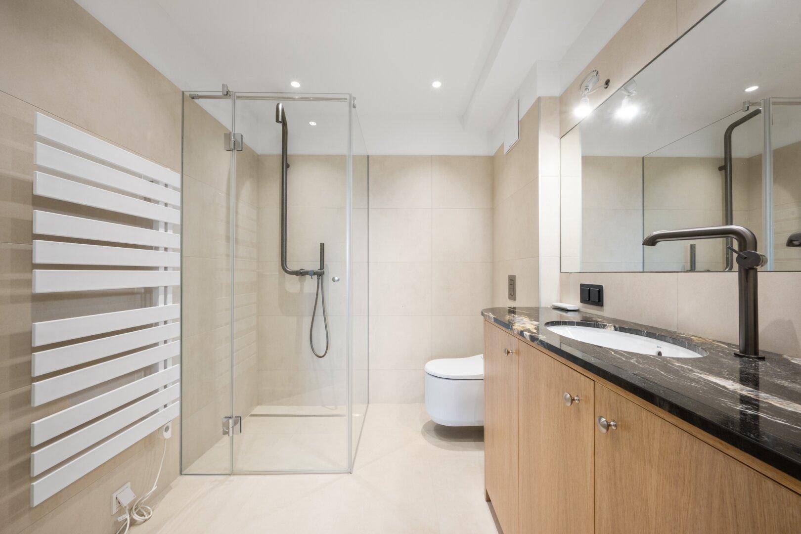Modernes Badezimmer mit begehbarer Dusche, dunkler Granitplatte und beheiztem Handtuchhalter.
