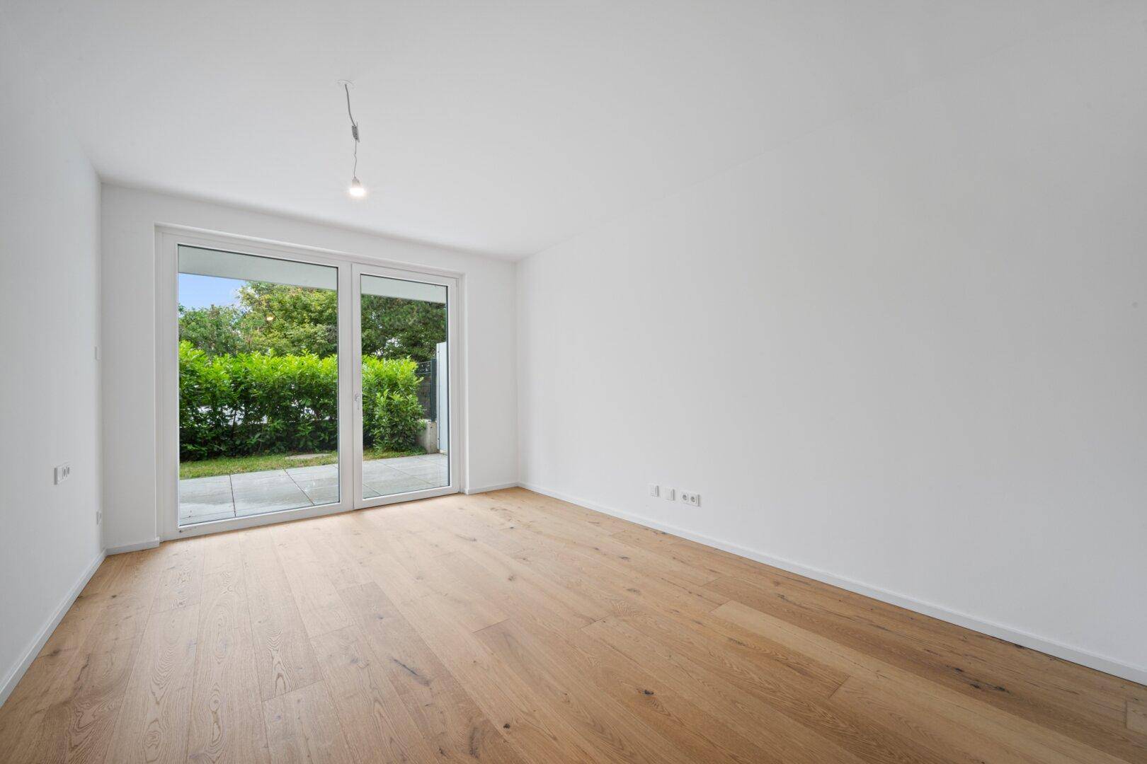 Weiteres helles Zimmer mit Holzboden und großen Fenstern mit Blick ins Grüne.
