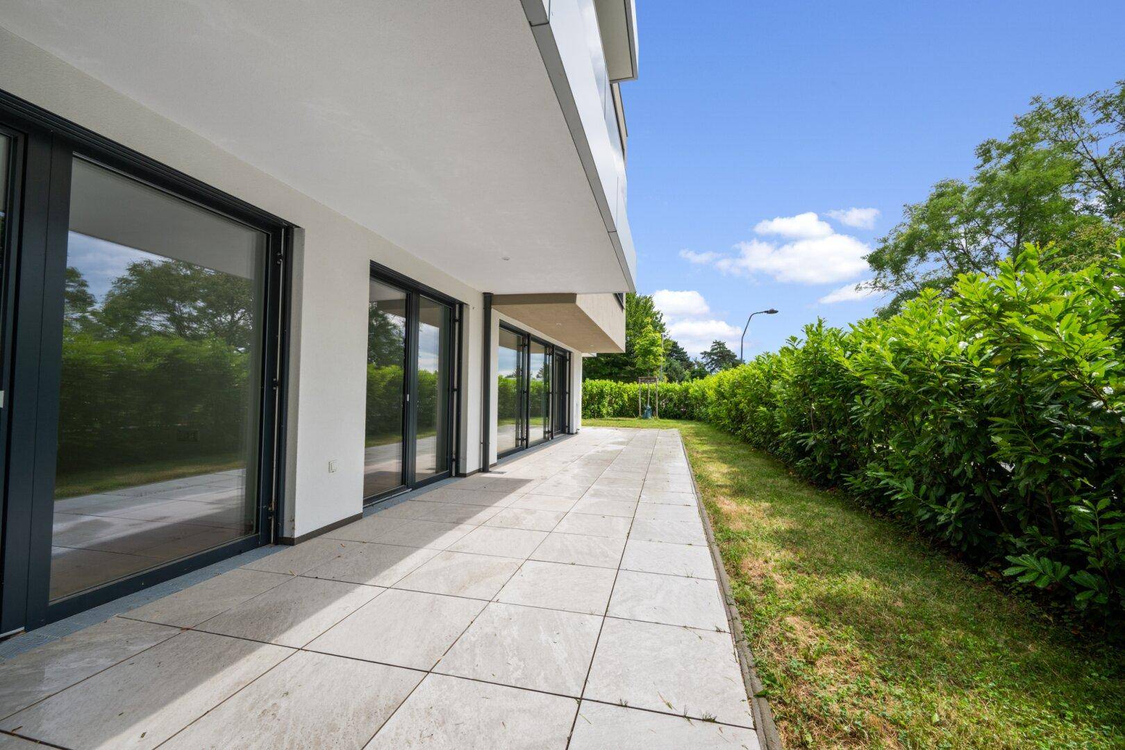Geräumige Terrasse mit großen Glasfronten und angrenzendem gepflegten Gartenbereich.