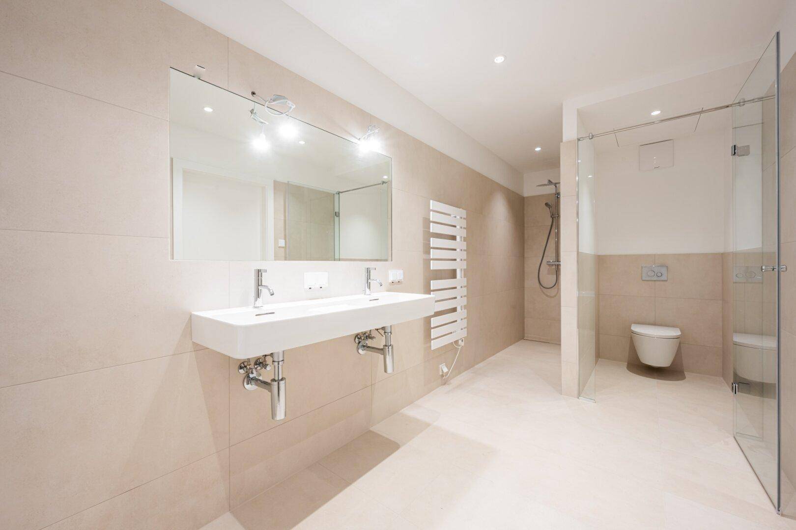 Modernes Badezimmer mit Doppelwaschbecken, großer Dusche und beheiztem Handtuchhalter.