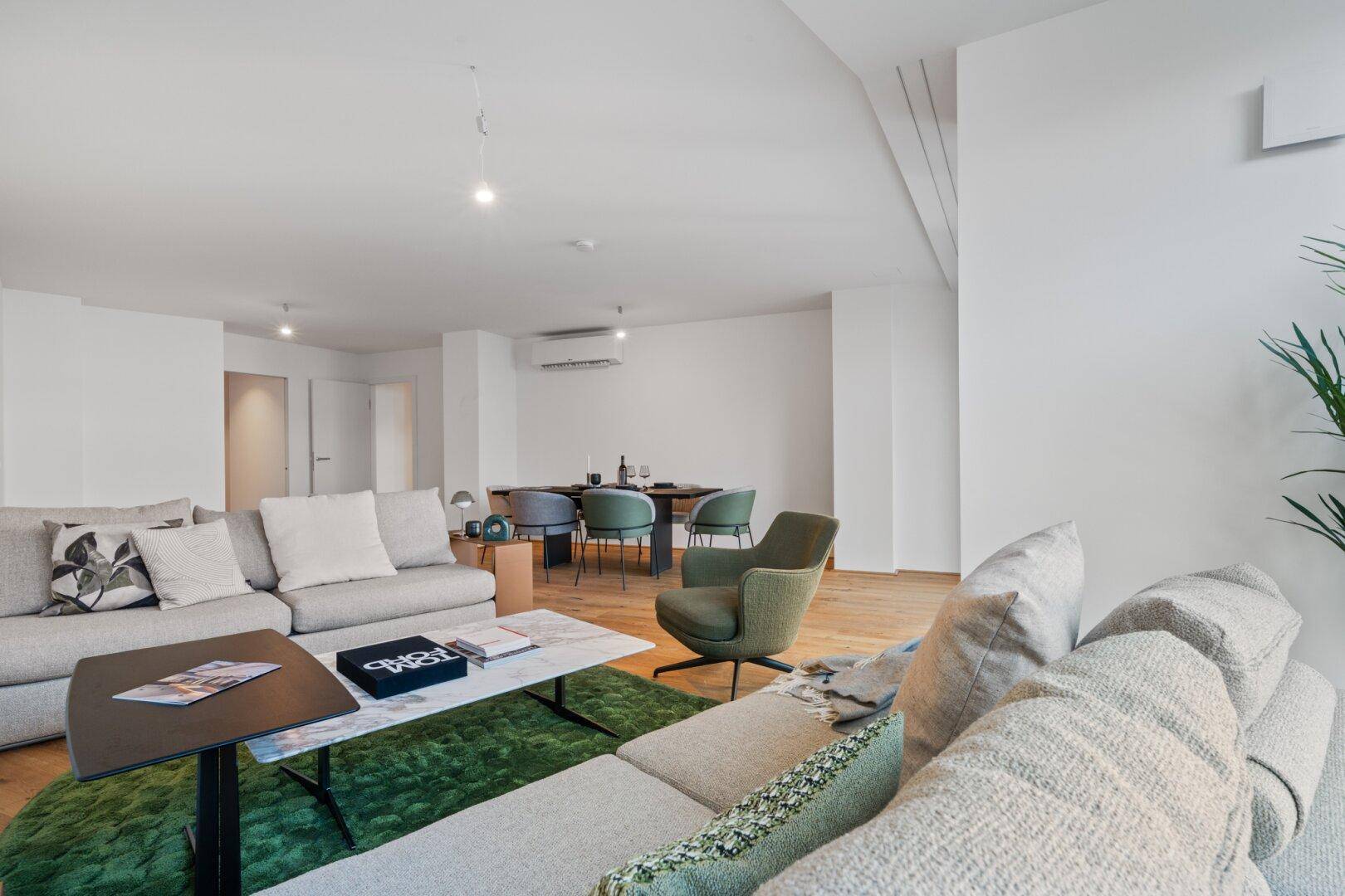 Geräumiger Wohn- und Essbereich mit großem Sofa, grünem Teppich und modernem Esstisch.