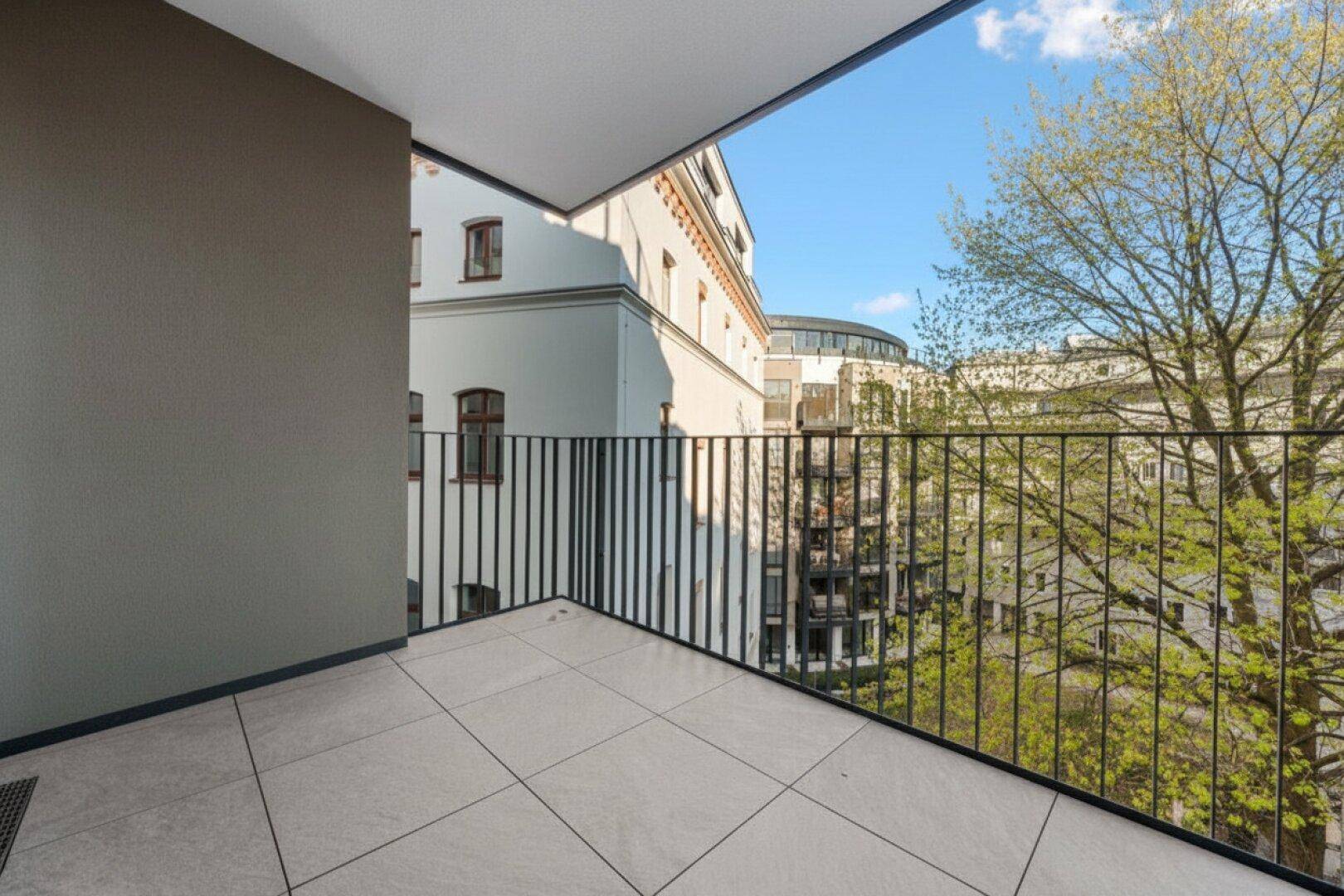 Geräumiger Balkon mit Fliesenboden und Blick auf die umliegenden Gebäude und Bäume.