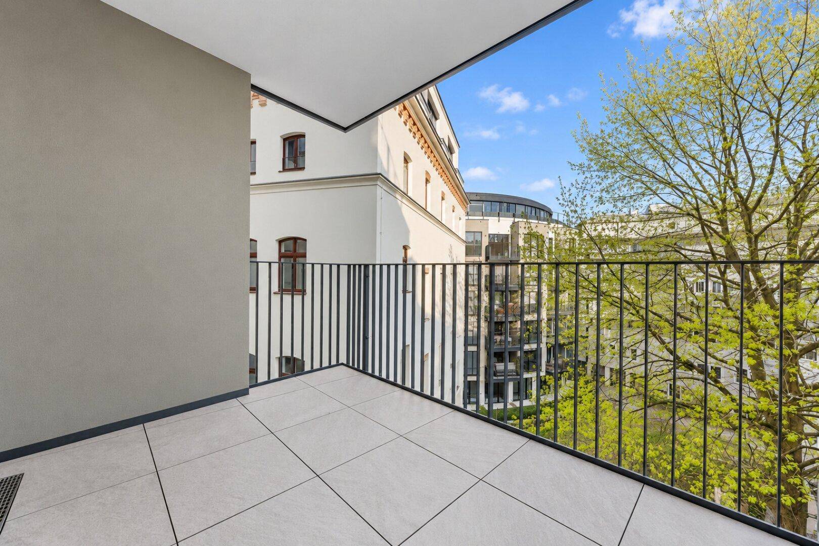 Heller Balkon mit Fliesenboden und Blick auf die umliegenden Gebäude und Bäume.